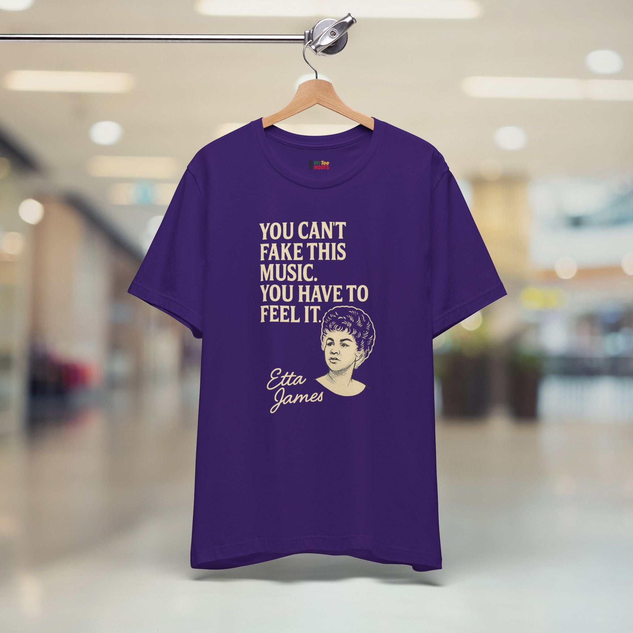 Purple t-shirt with text and graphic of Etta James on a hanger in a store.
