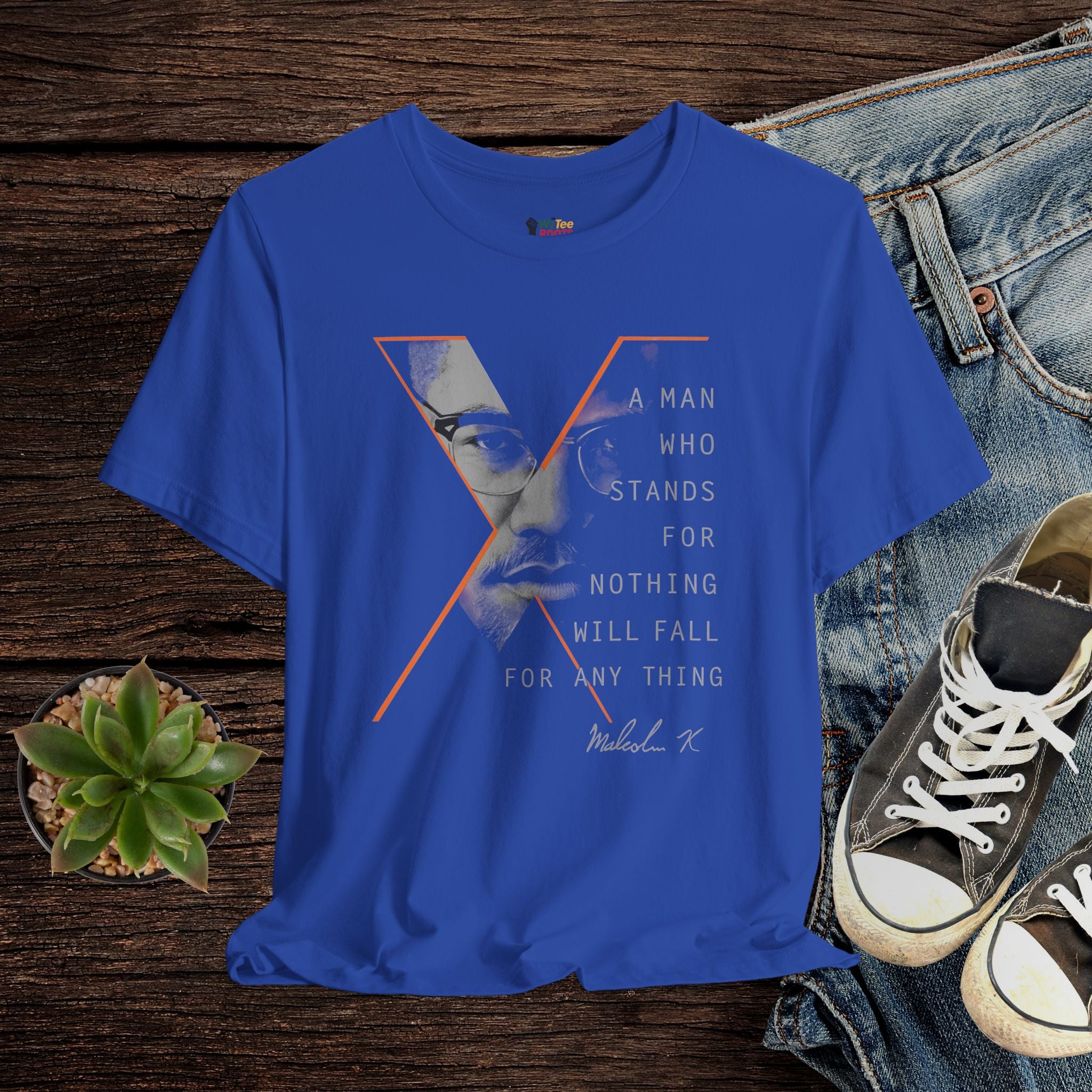 Blue t-shirt with graphic design and text on a wooden surface with jeans and sneakers.
