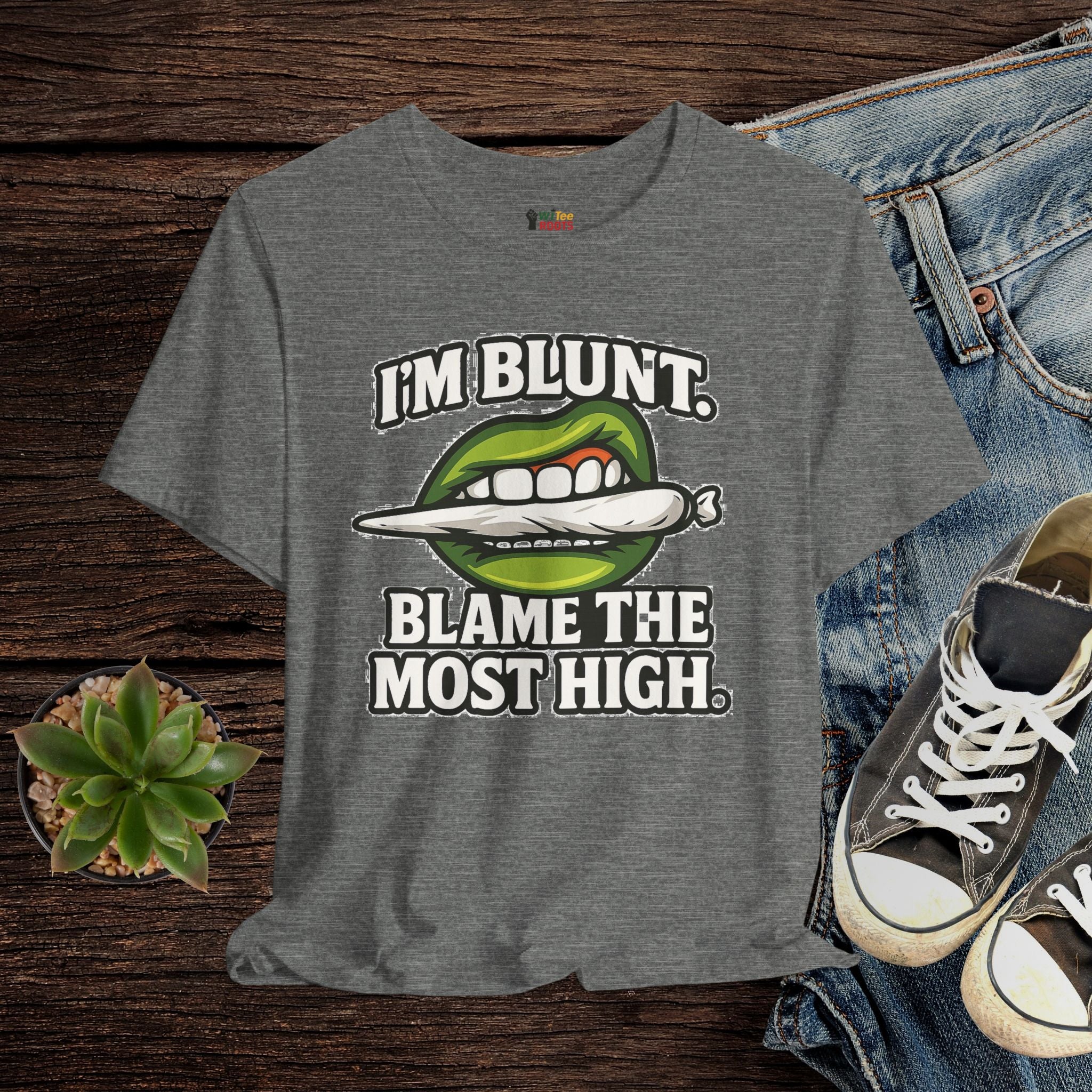 Gray t-shirt with graphic design and text on a wooden surface with jeans and sneakers.