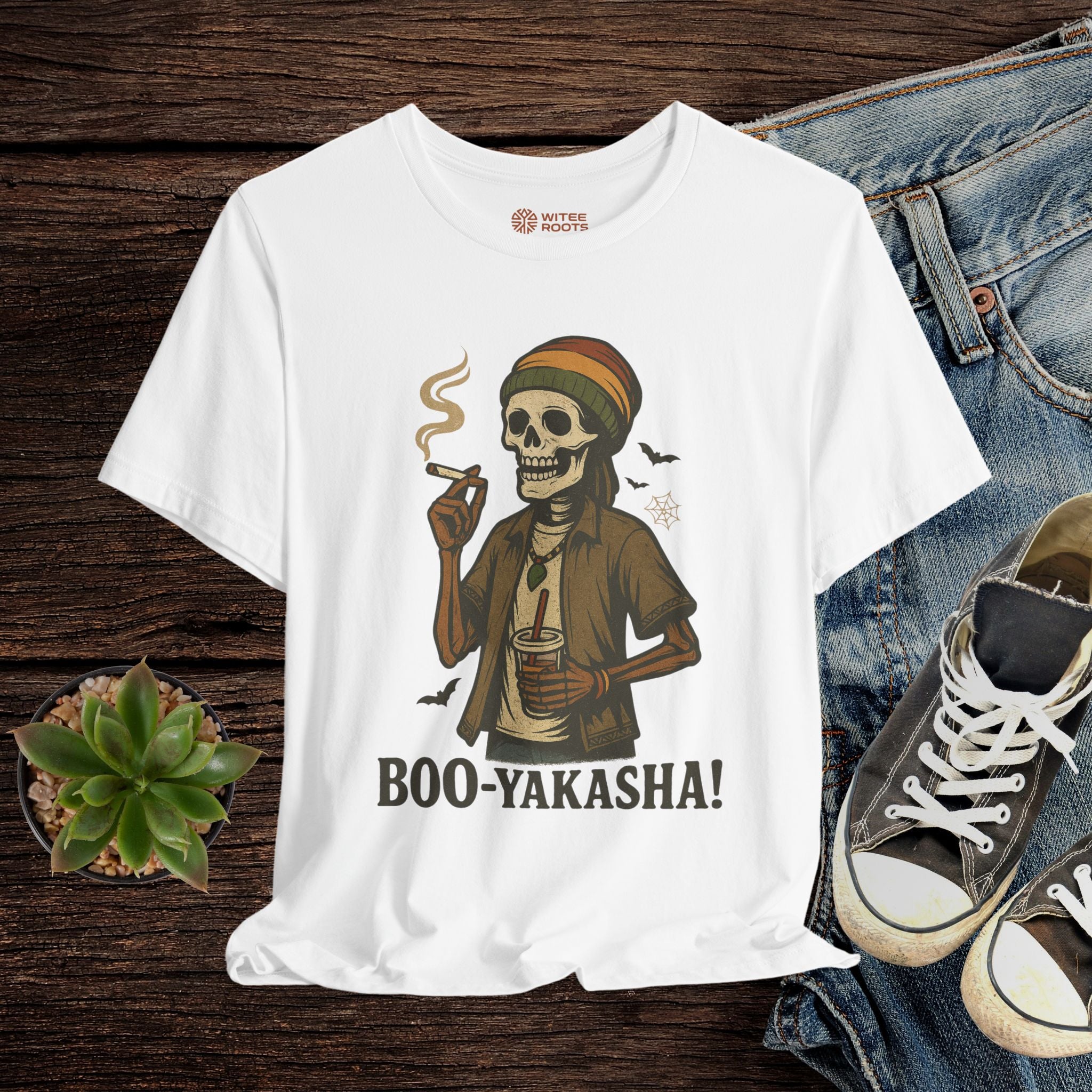 White t-shirt with a skeleton smoking and holding a drink, labeled 'BOO-YAKASHA!', displayed on a wooden surface with jeans and sneakers.