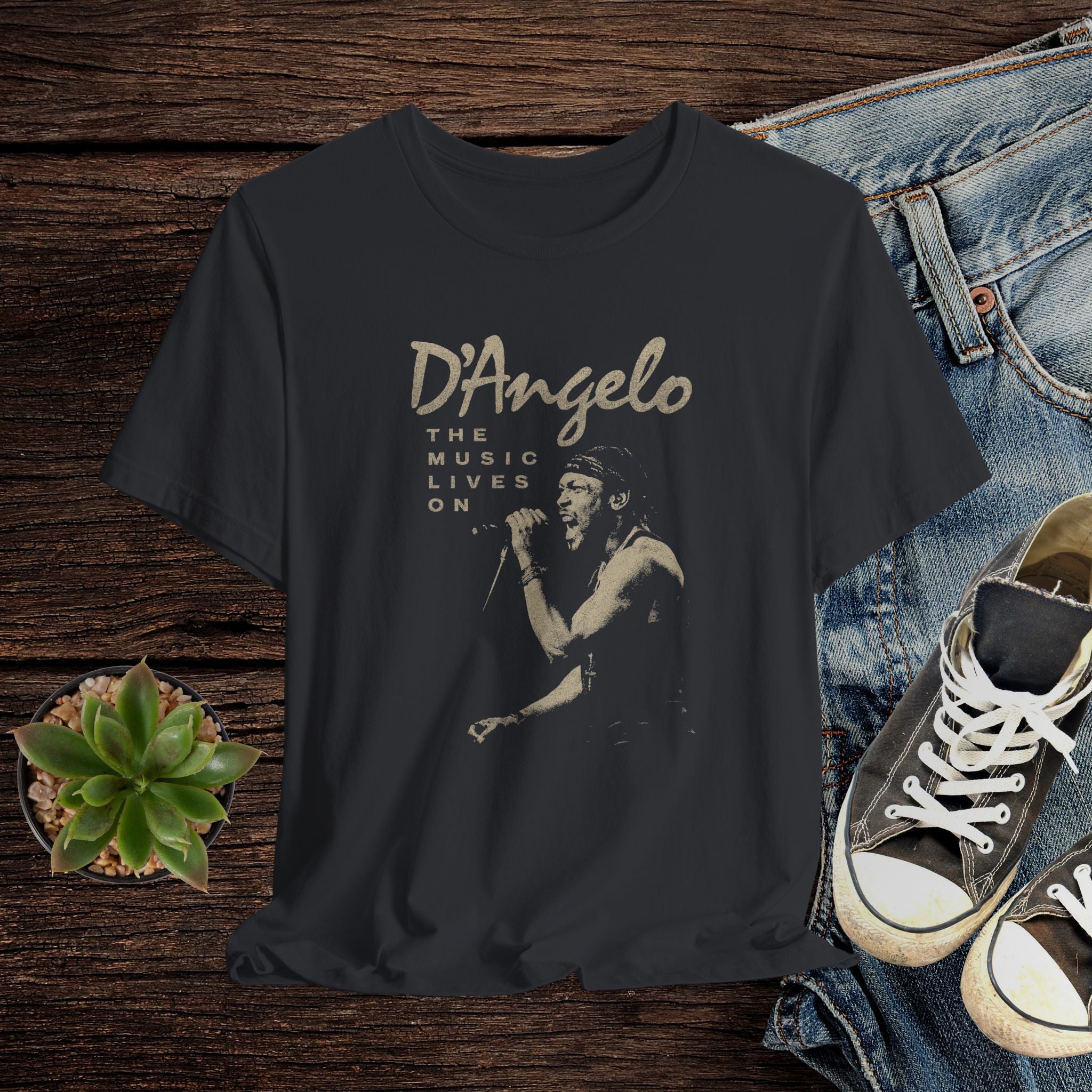 Black t-shirt with D'Angelo graphic design on a wooden surface with jeans and sneakers.