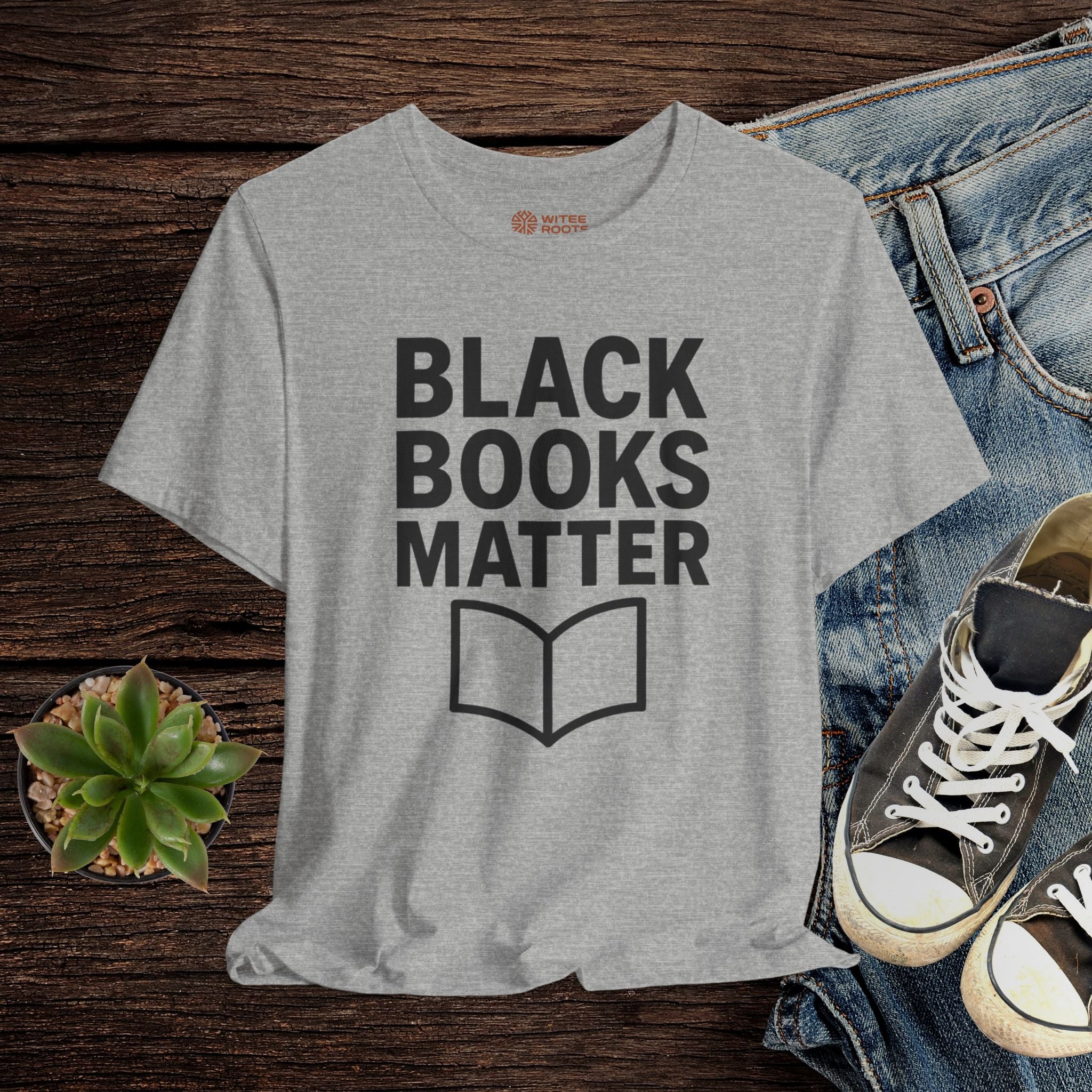 Gray t-shirt with 'Black Books Matter' text on a wooden surface with jeans and sneakers.