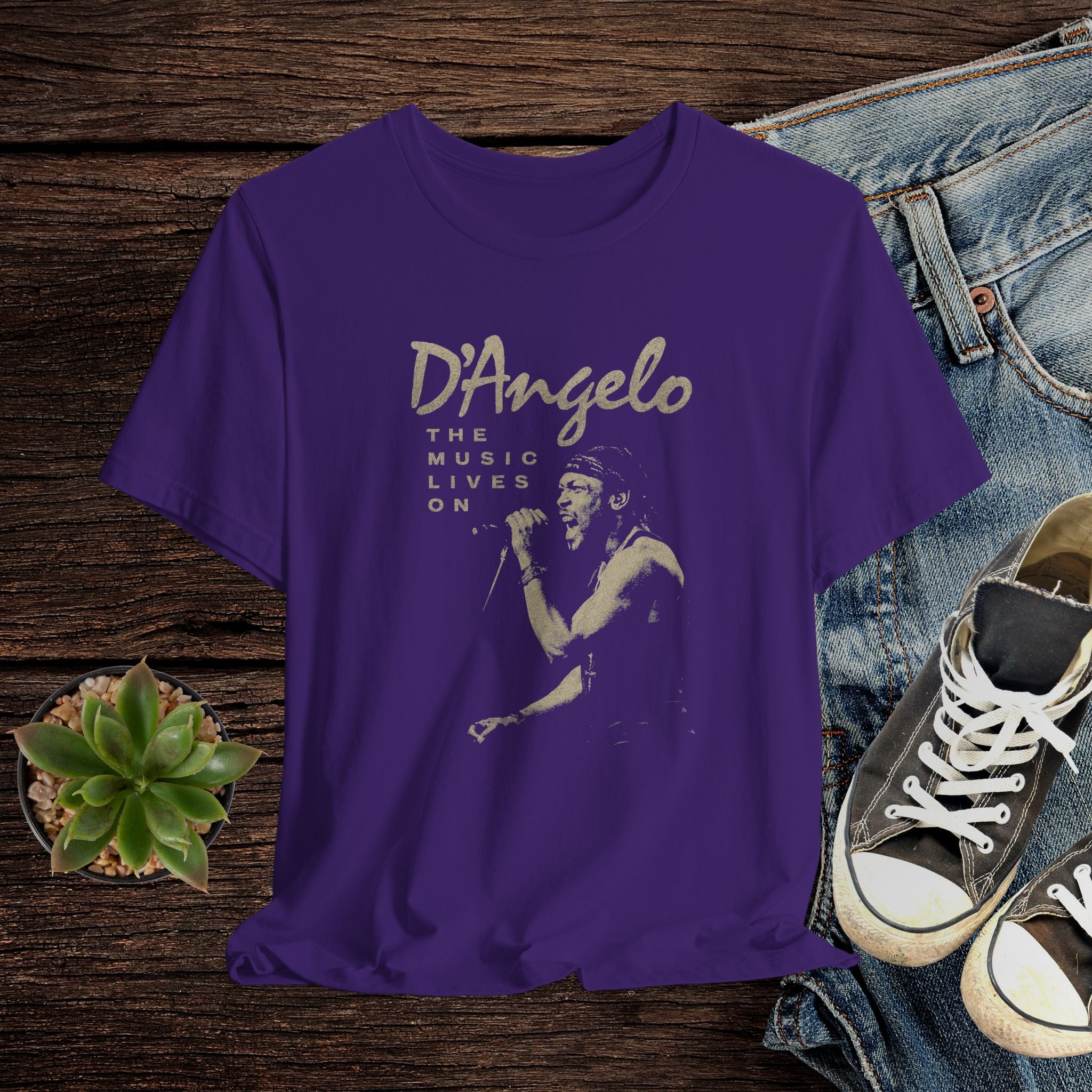 Purple t-shirt with D'Angelo graphic design on a wooden surface with jeans and sneakers.