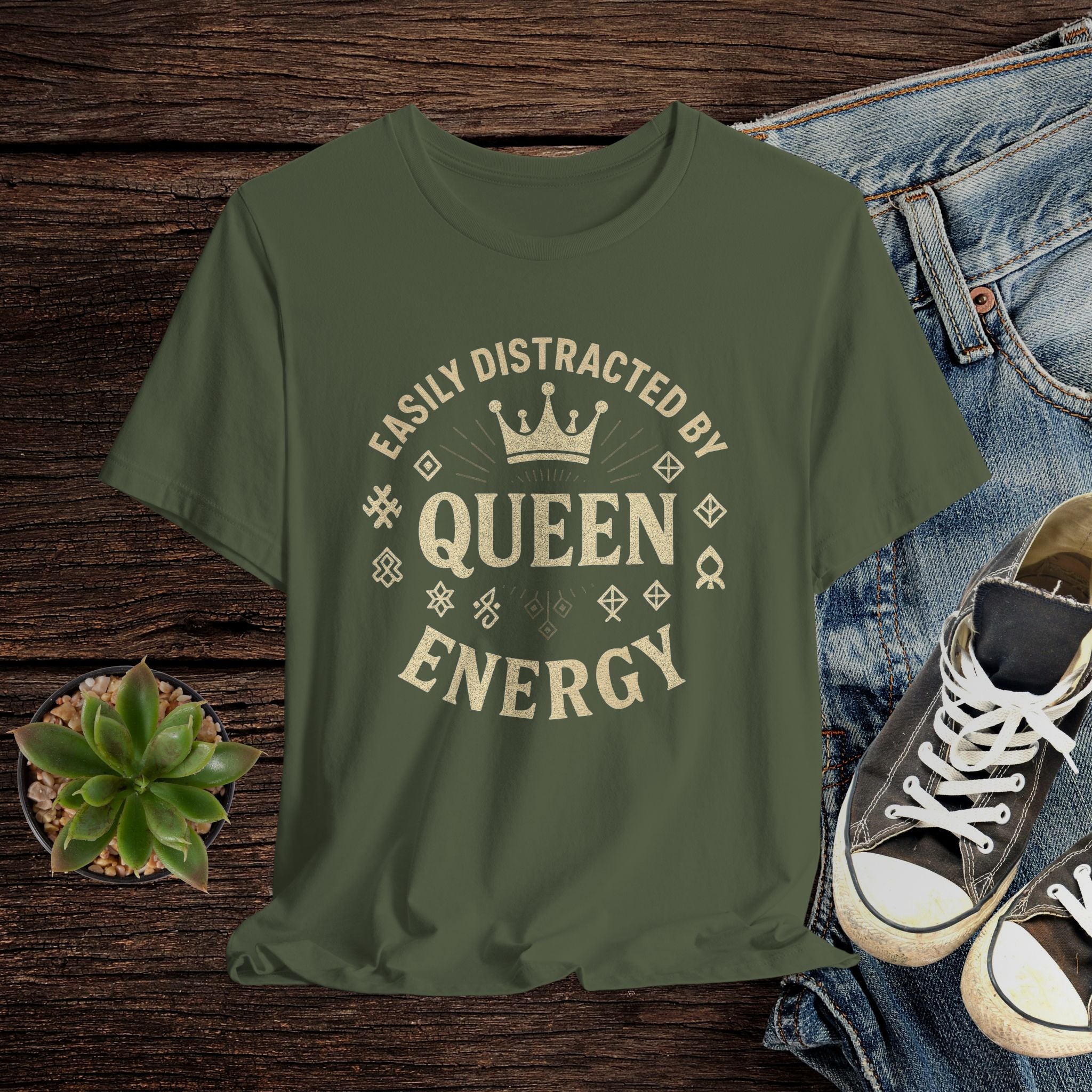 Green t-shirt with 'Easily Distracted by Queen Energy' text on a wooden surface with jeans and sneakers.