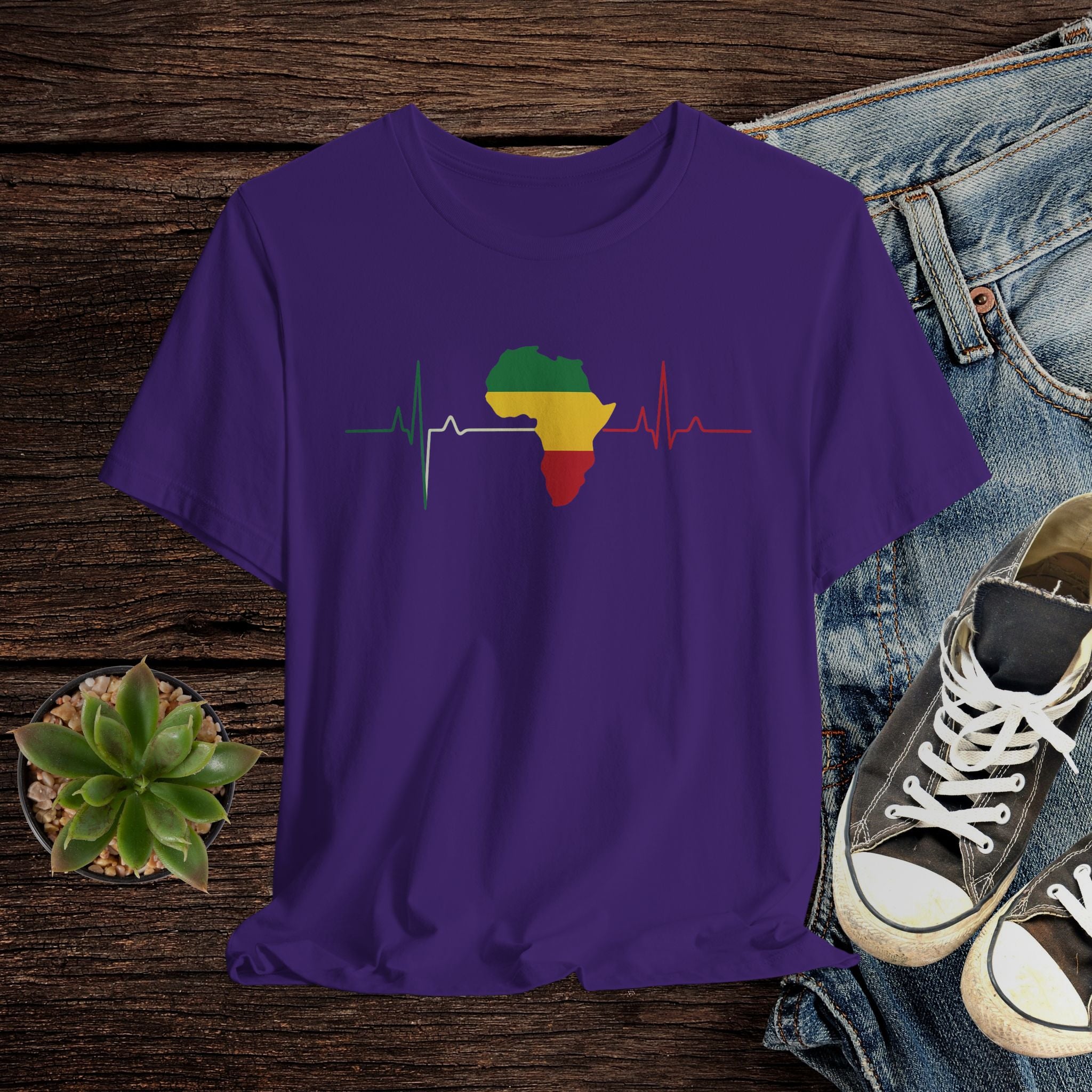 Purple t-shirt with a colorful Africa map design on a wooden surface with jeans and sneakers.