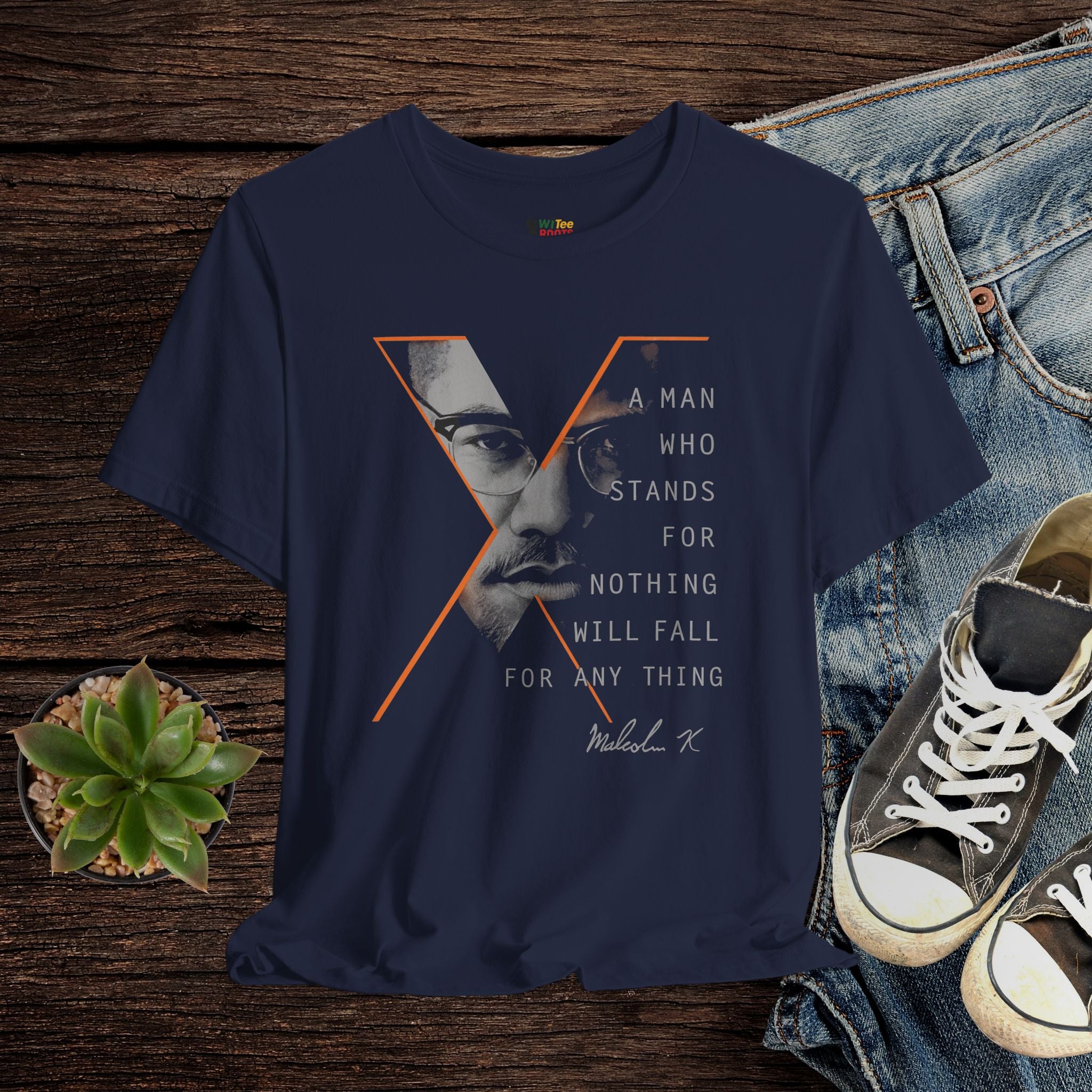 Navy blue t-shirt with graphic design and text on a wooden surface with jeans and sneakers.