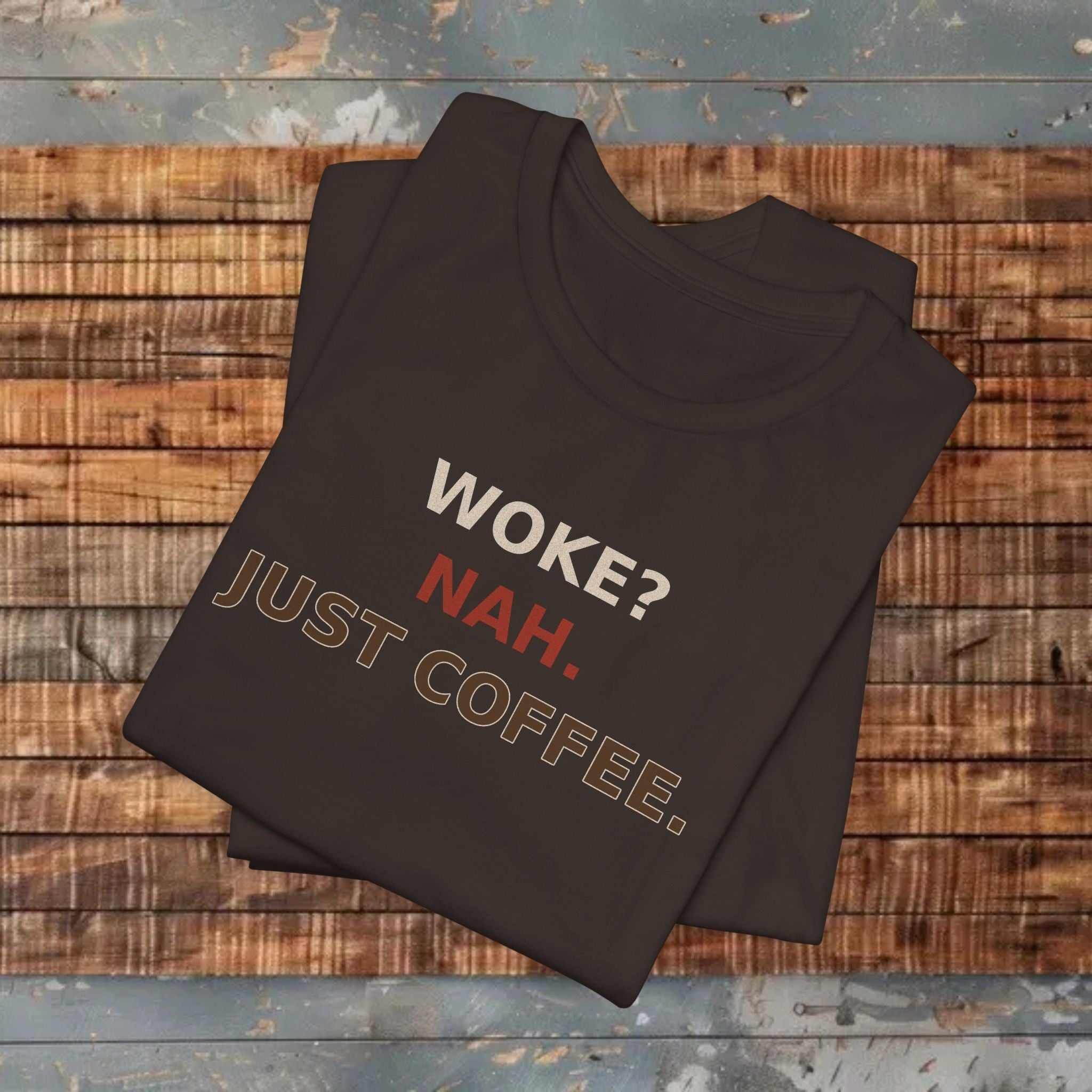 Folded brown t-shirt with text 'WOKE? NAH. JUST COFFEE.' on a wooden surface