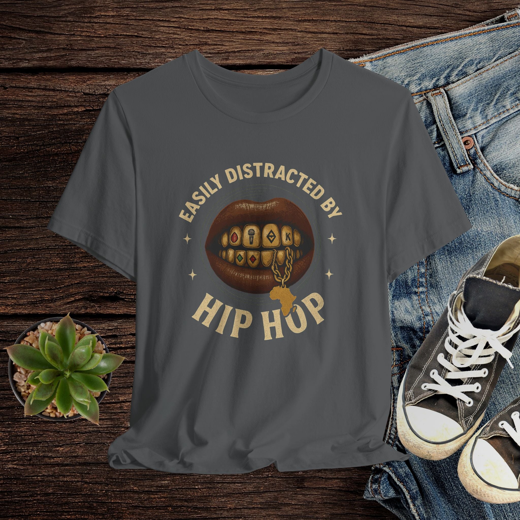 Gray t-shirt with 'Easily Distracted by Hip Hop' graphic on a wooden surface with jeans and sneakers.