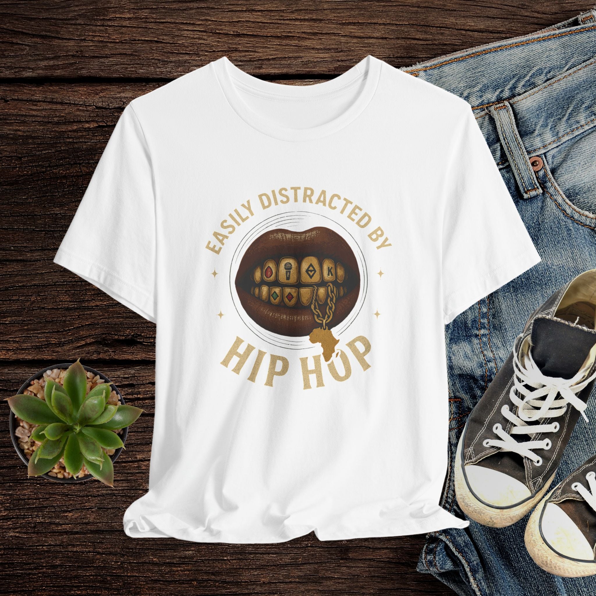 White t-shirt with 'Easily Distracted by Hip Hop' graphic on a wooden surface with jeans and sneakers.