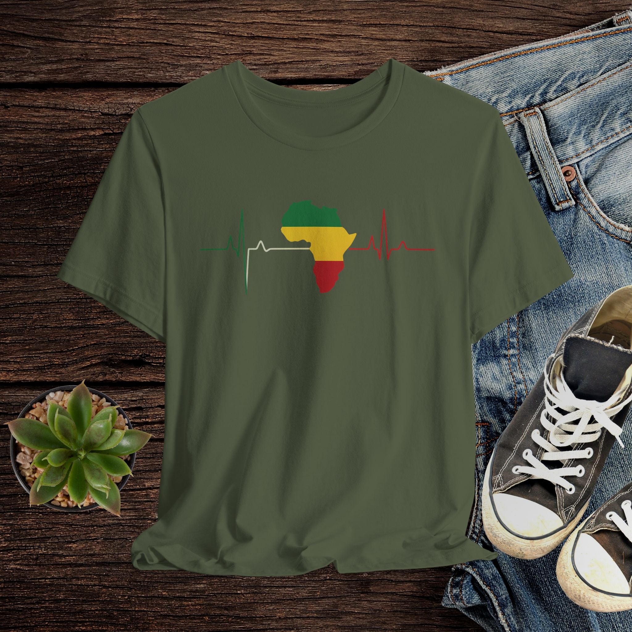Green t-shirt with Africa map and heartbeat design on a wooden surface with jeans and sneakers.