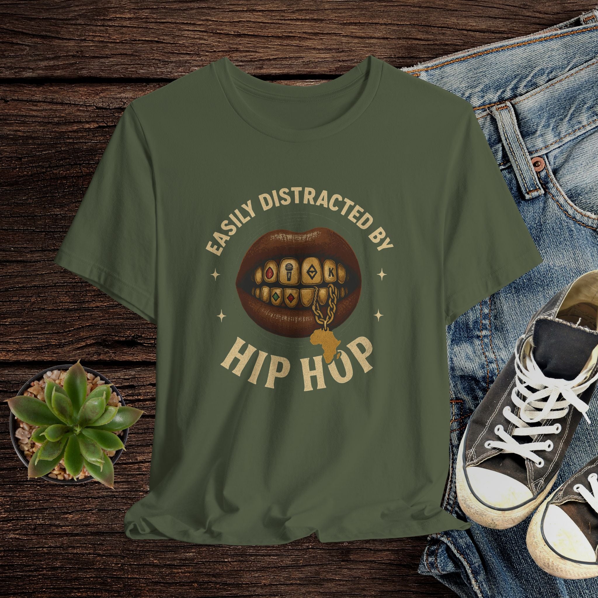Green t-shirt with 'Easily Distracted by Hip Hop' graphic on a wooden surface with jeans and sneakers.