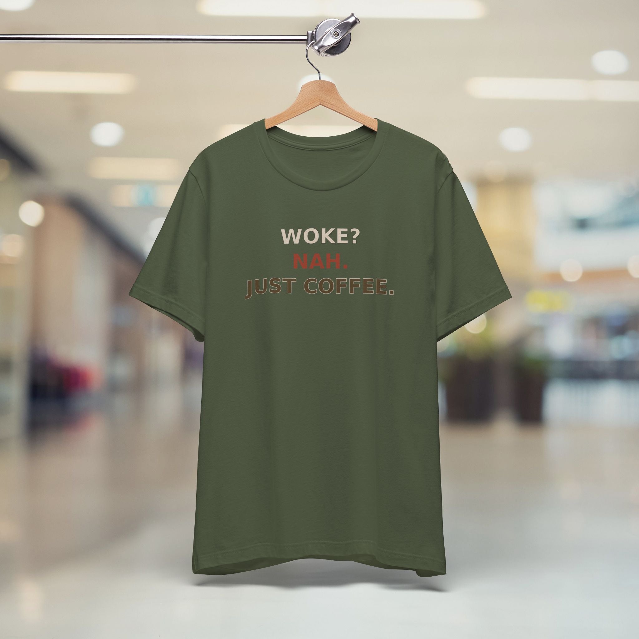 Green t-shirt with text 'Woke? Nah. Just Coffee.' on a hanger in a store setting.