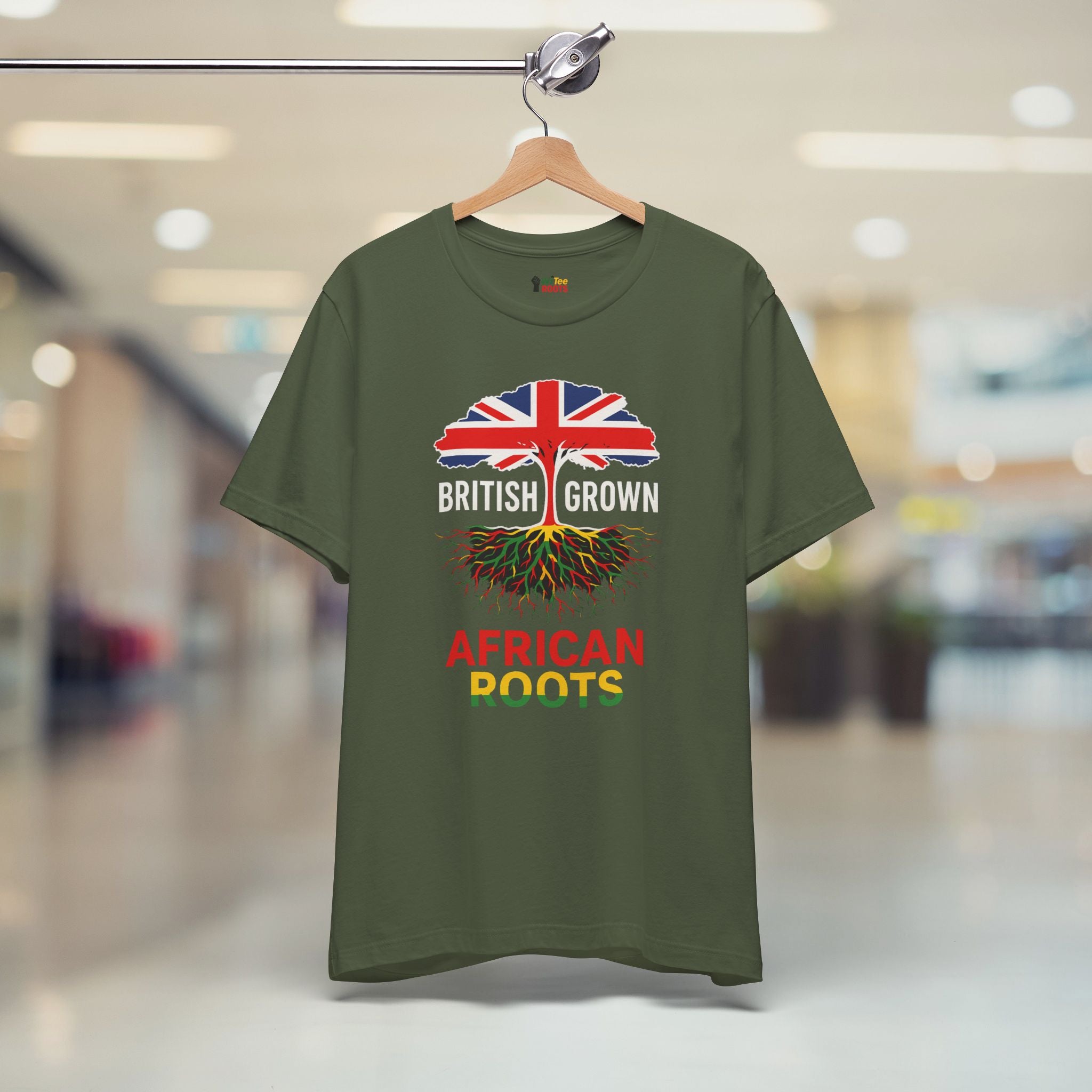 Green t-shirt with 'British Grown African Roots' design on a hanger in a store.