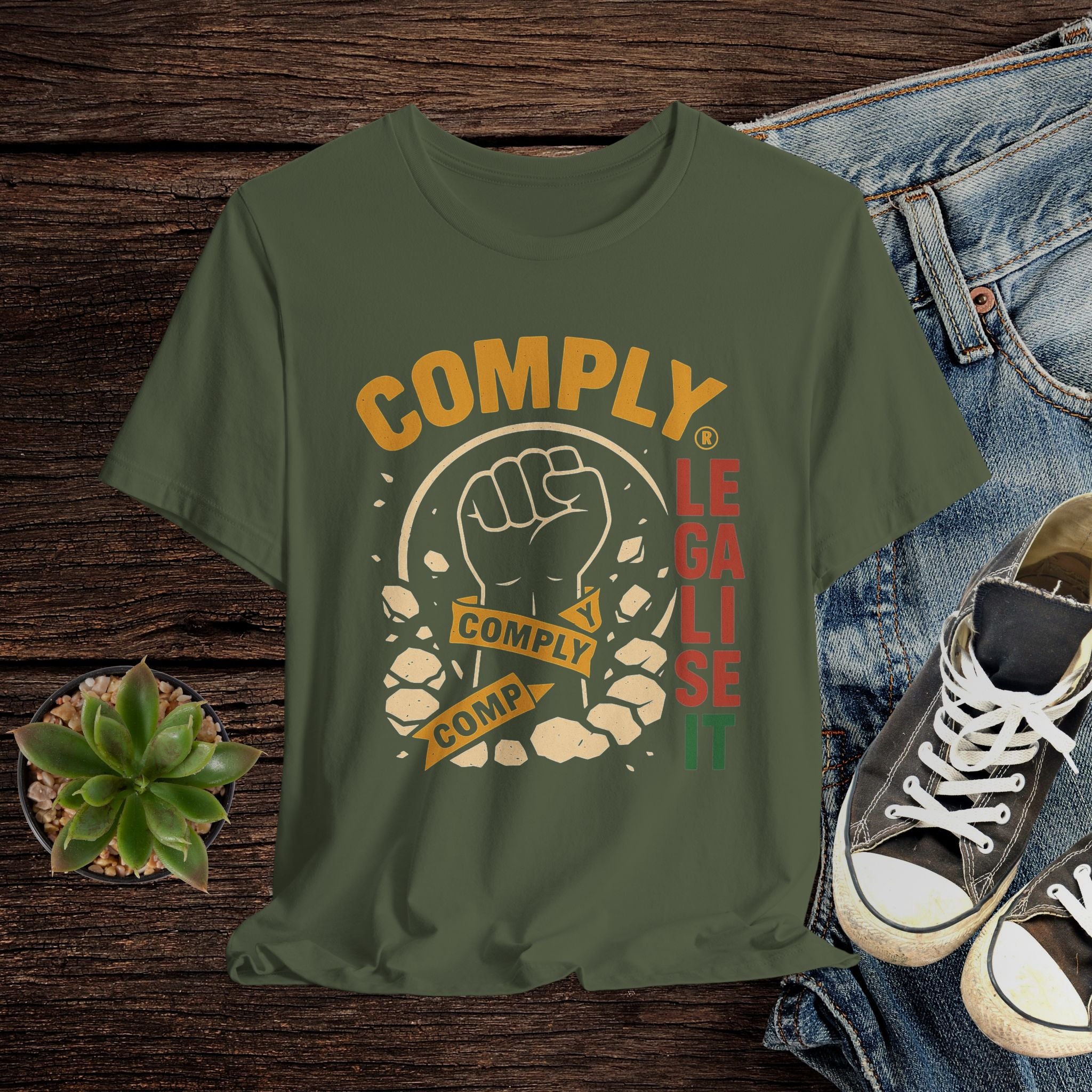 Green t-shirt with graphic design featuring a fist and text on a wooden surface with jeans and shoes.