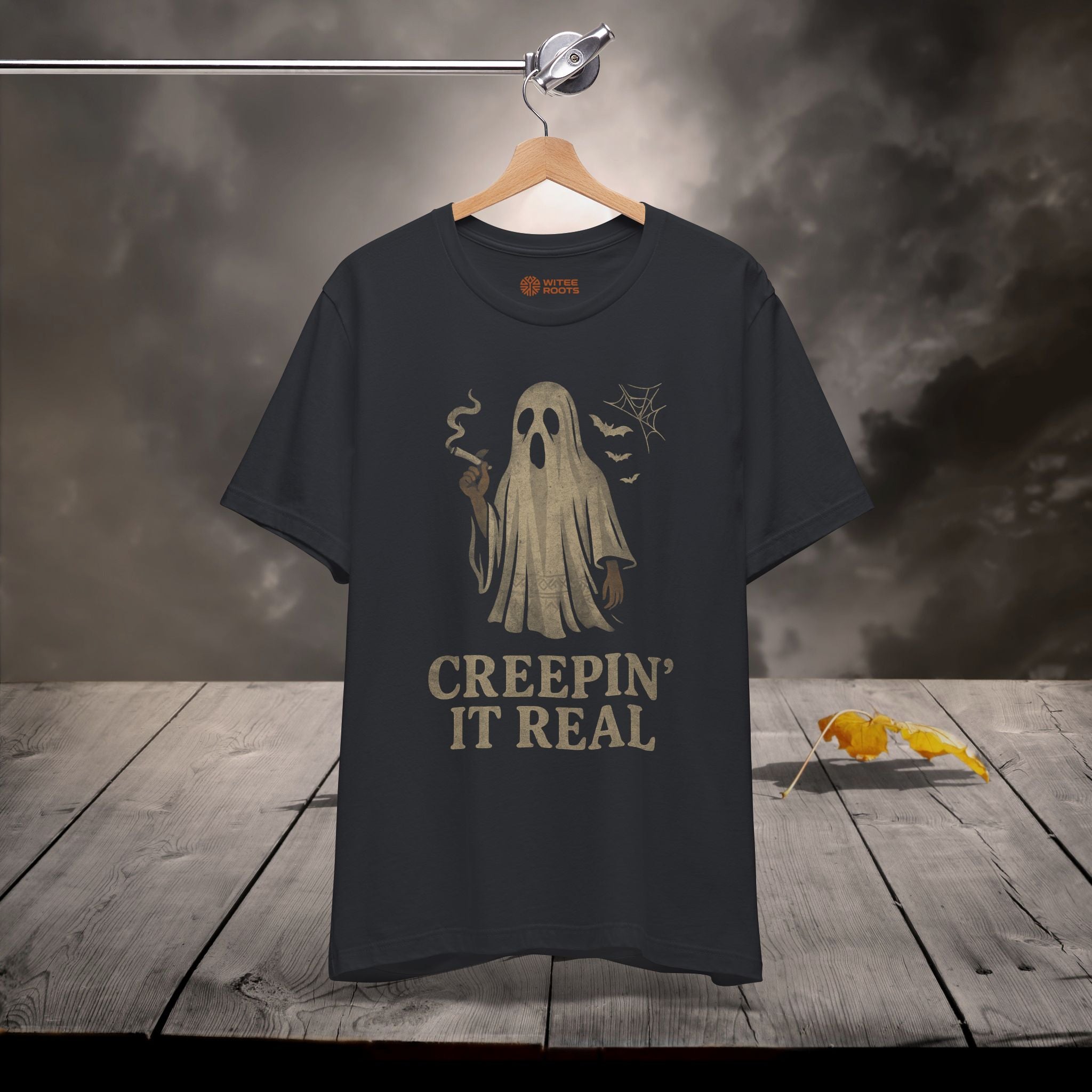 Black t-shirt with ghost graphic and text 'Creepin' It Real' on a wooden surface with dark background