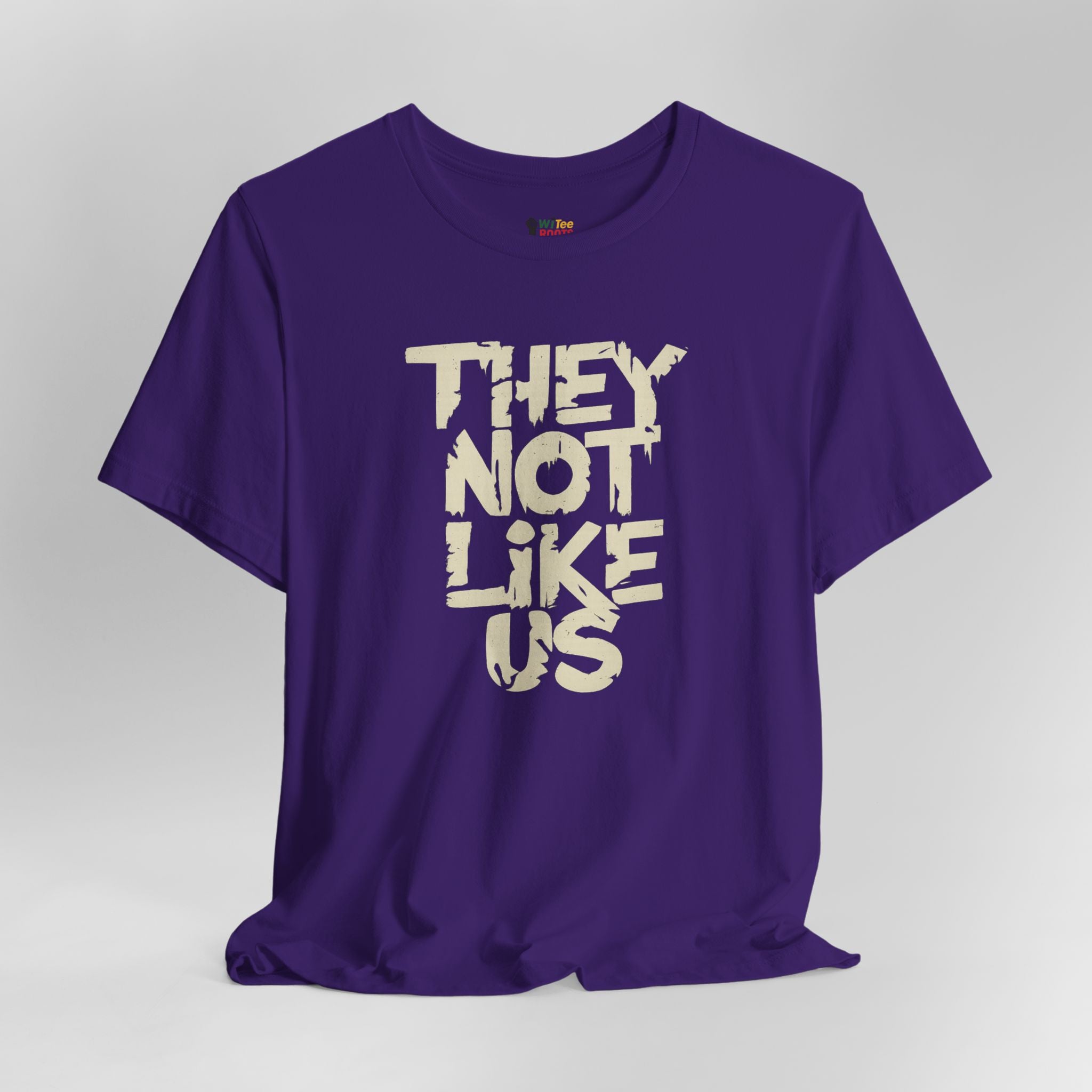 Purple t-shirt with white text 'THEY NOT LIKE US' on a gray background