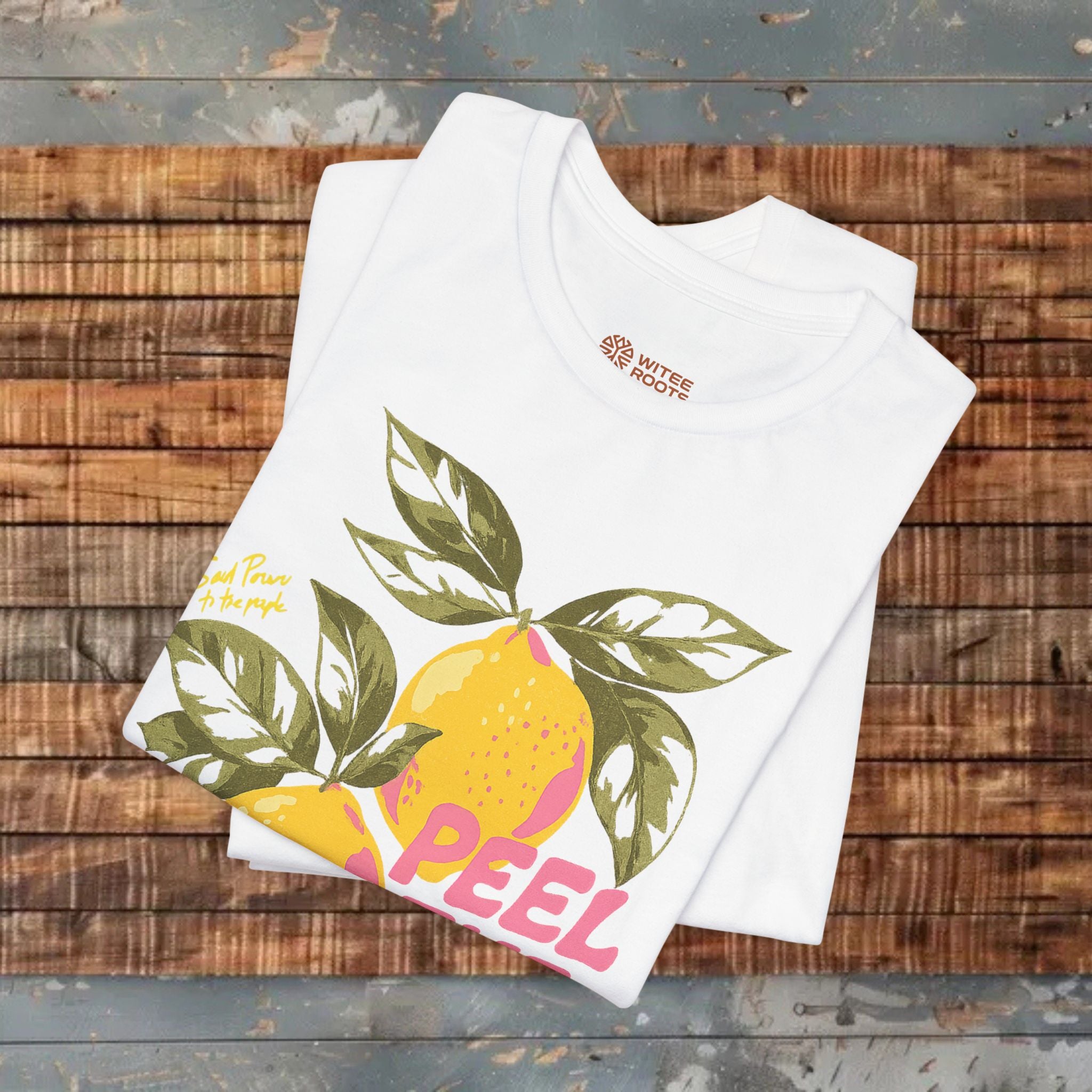 White t-shirt with lemon graphic and 'PEEL' text on a wooden surface