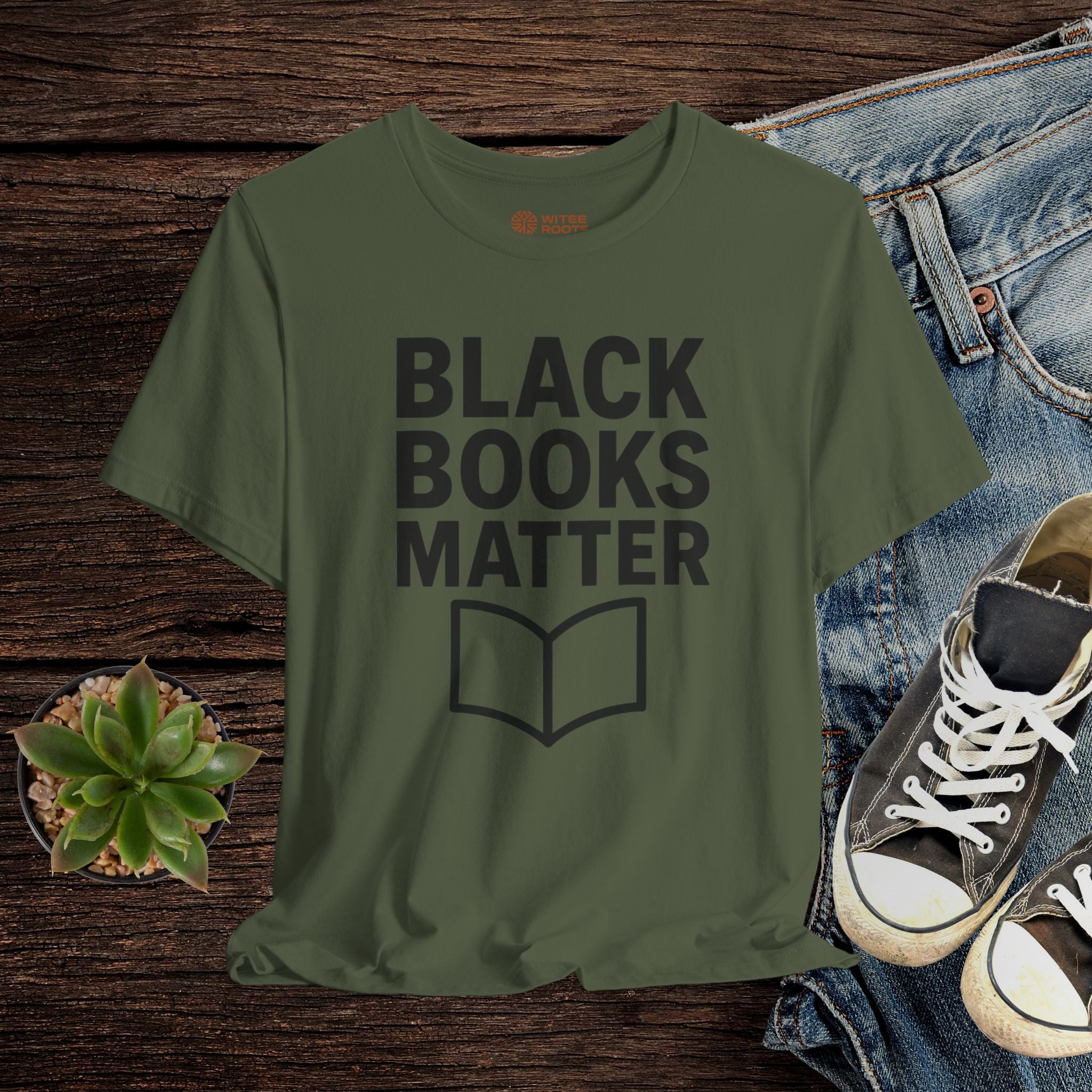 Green t-shirt with 'BLACK BOOKS MATTER' text on a wooden surface with jeans and sneakers.
