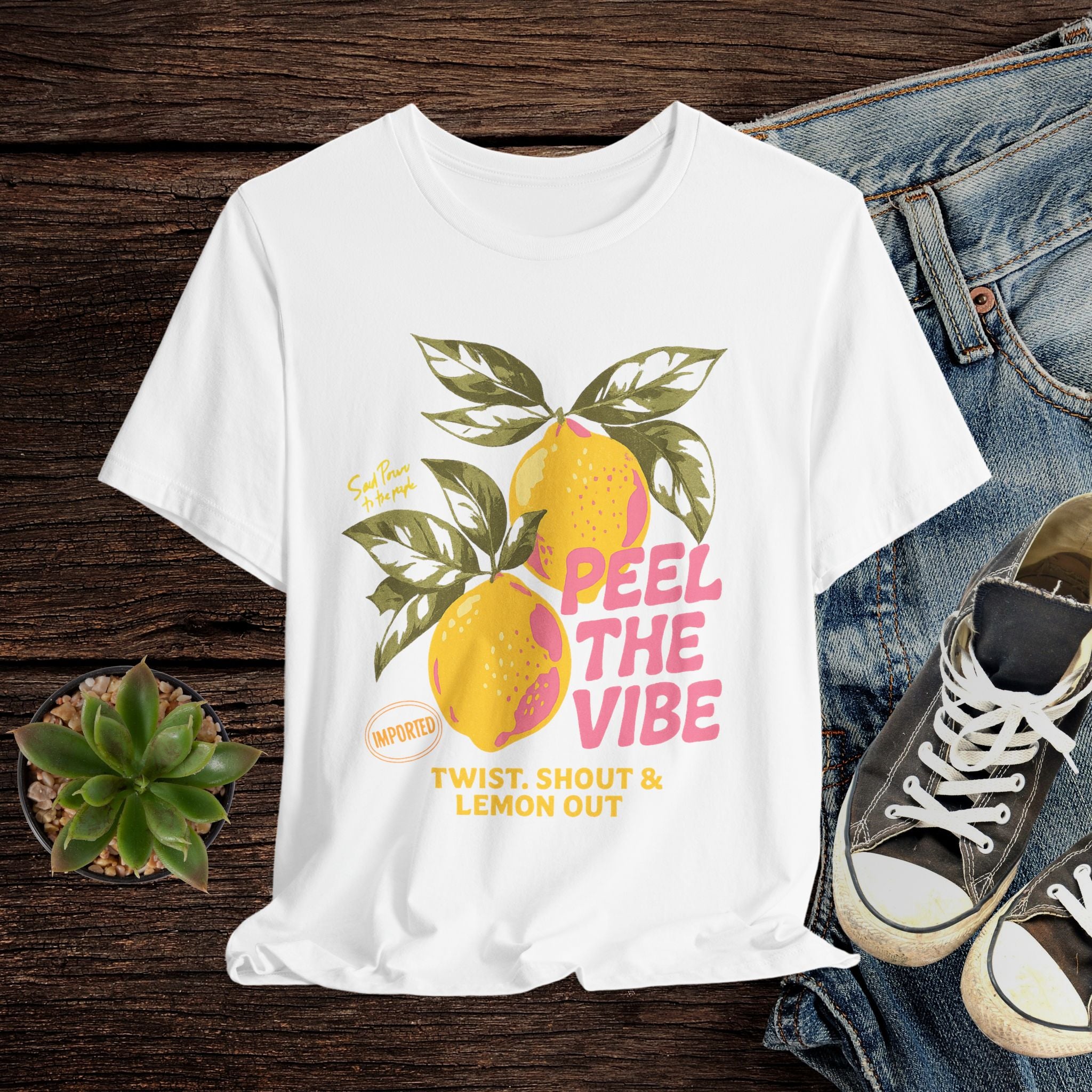 White t-shirt with lemon graphic and text on a wooden surface with jeans and sneakers.