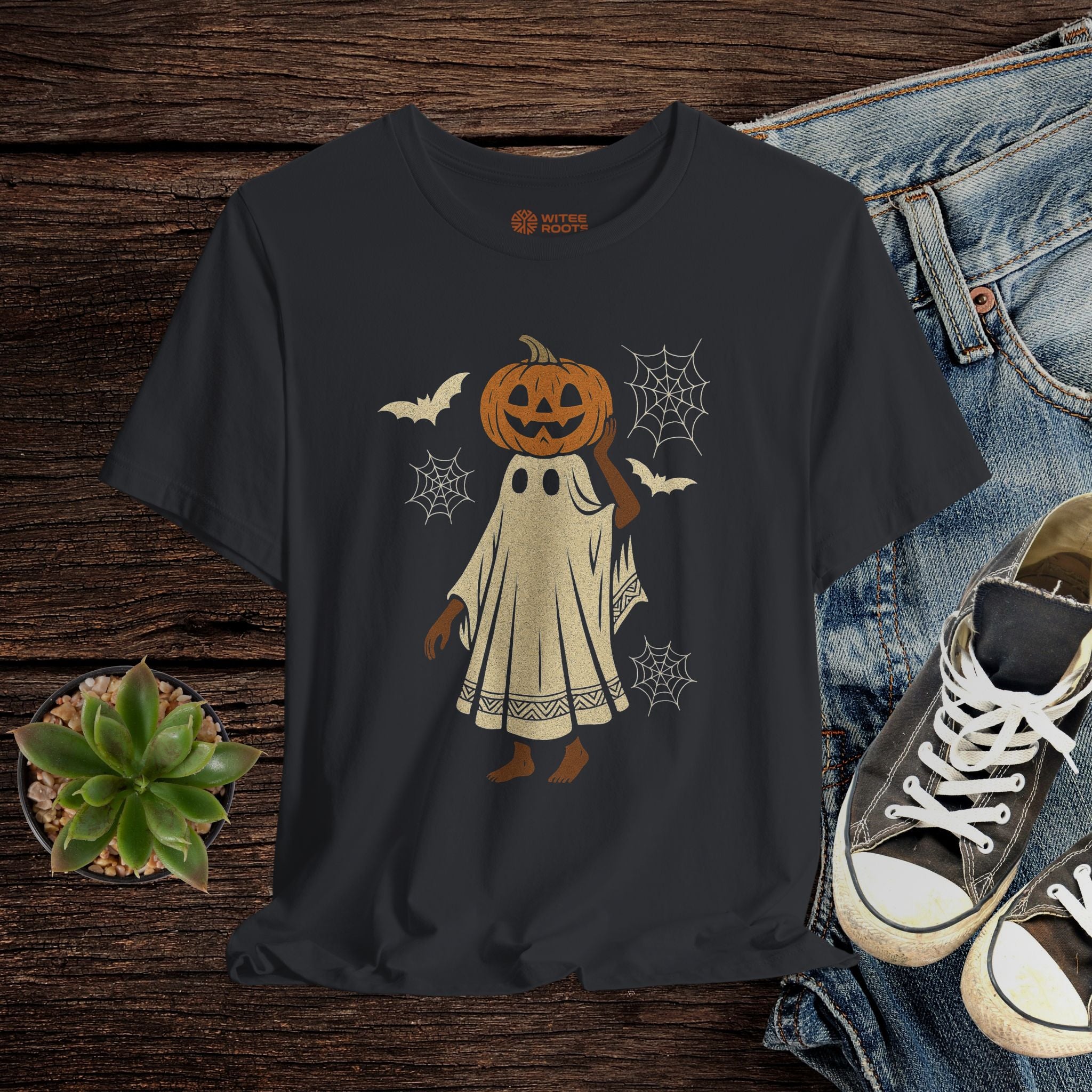 Black t-shirt with a pumpkin ghost design on a wooden surface with jeans and sneakers.