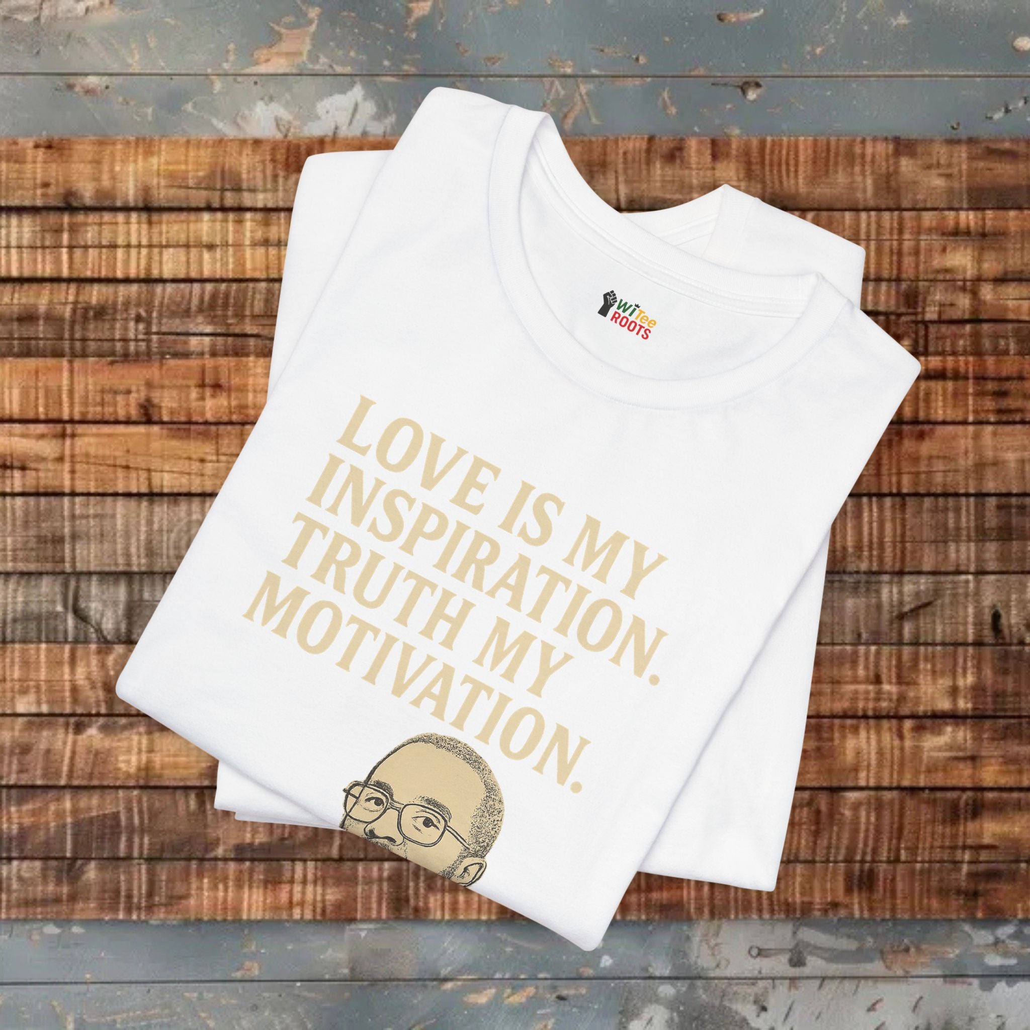 White t-shirt with gold text and logo on a wooden surface