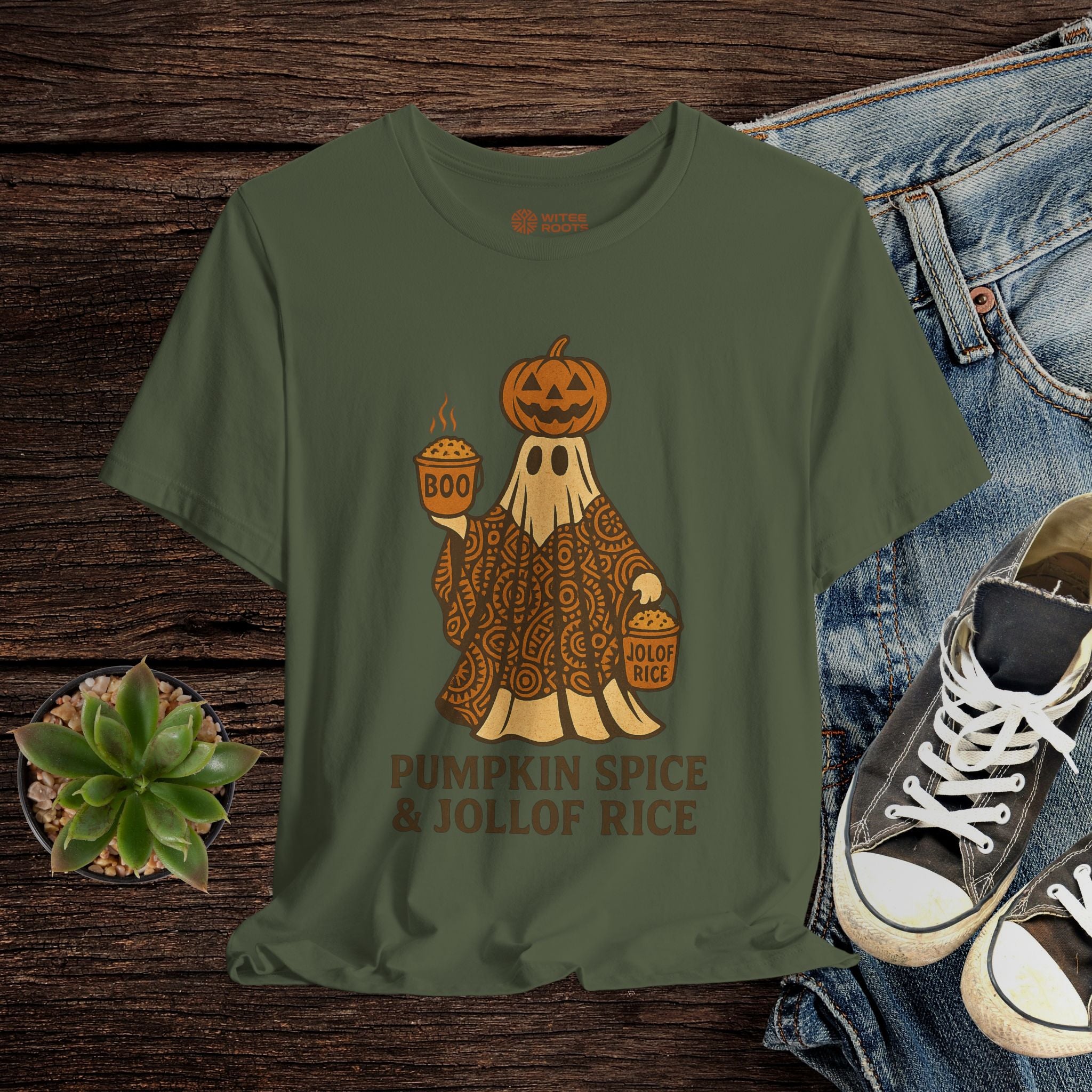 Green t-shirt with ghost and pumpkin design, placed on a wooden surface with jeans and sneakers.