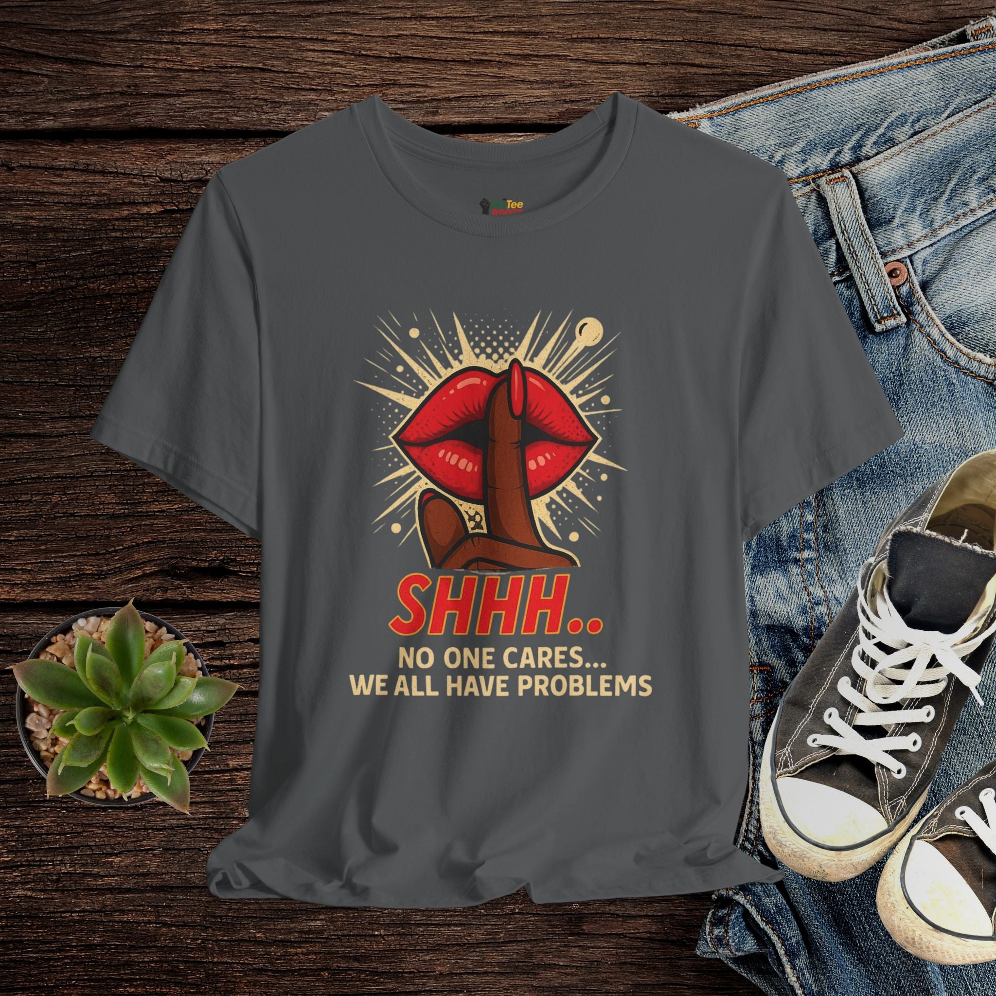 Gray t-shirt with graphic design and text on a wooden surface with jeans and sneakers.