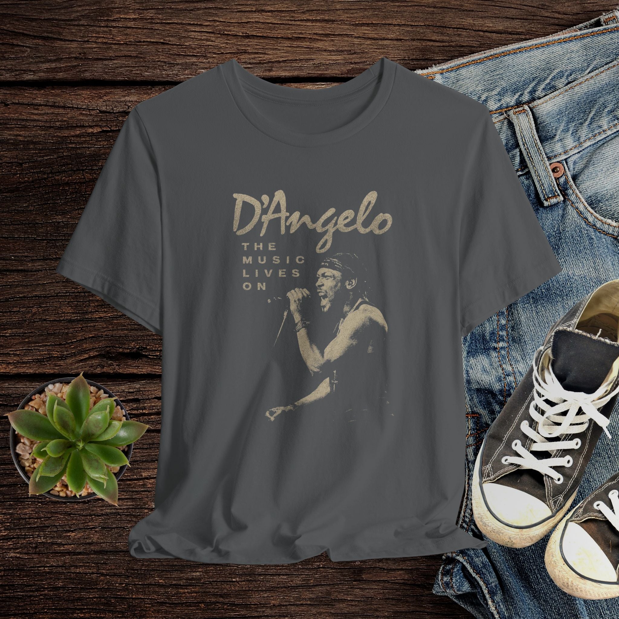 Gray t-shirt with D'Angelo graphic design on a wooden surface with jeans and sneakers.