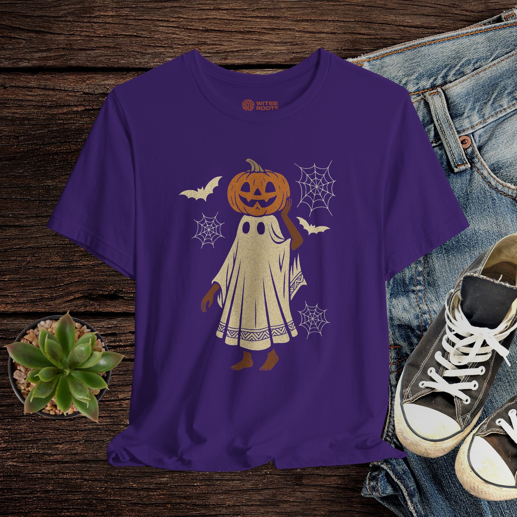 Purple t-shirt with Halloween-themed design on a wooden surface with jeans and shoes.