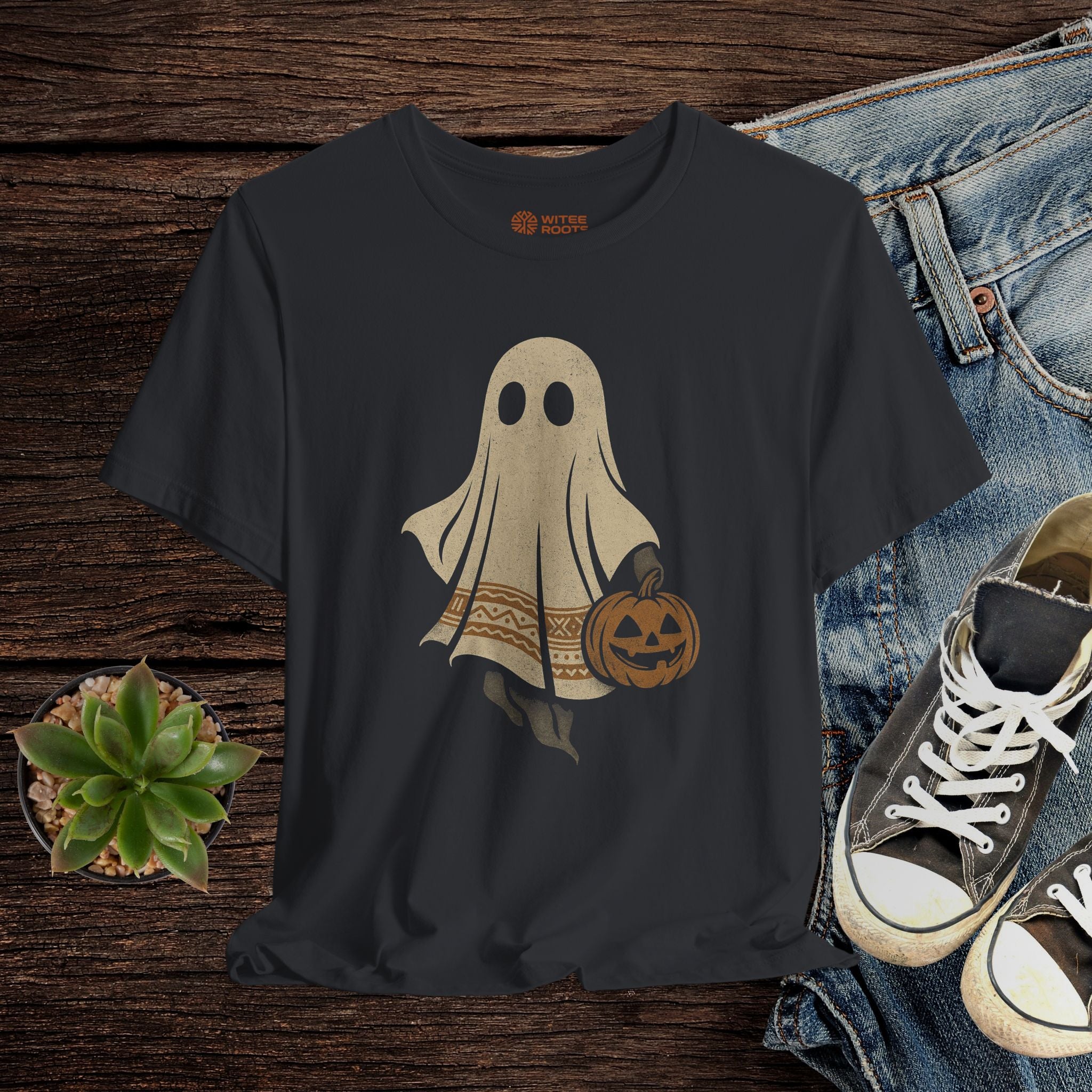 Black t-shirt with ghost and pumpkin design on a wooden surface with jeans and sneakers.