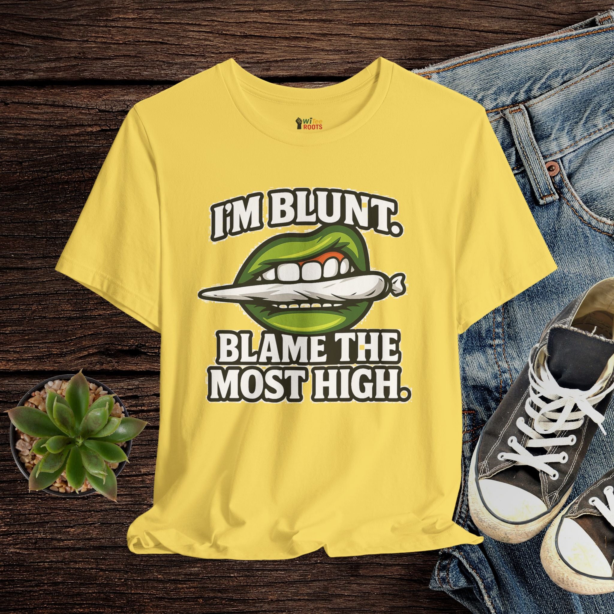 Yellow t-shirt with graphic design and text on a wooden surface with jeans and sneakers.