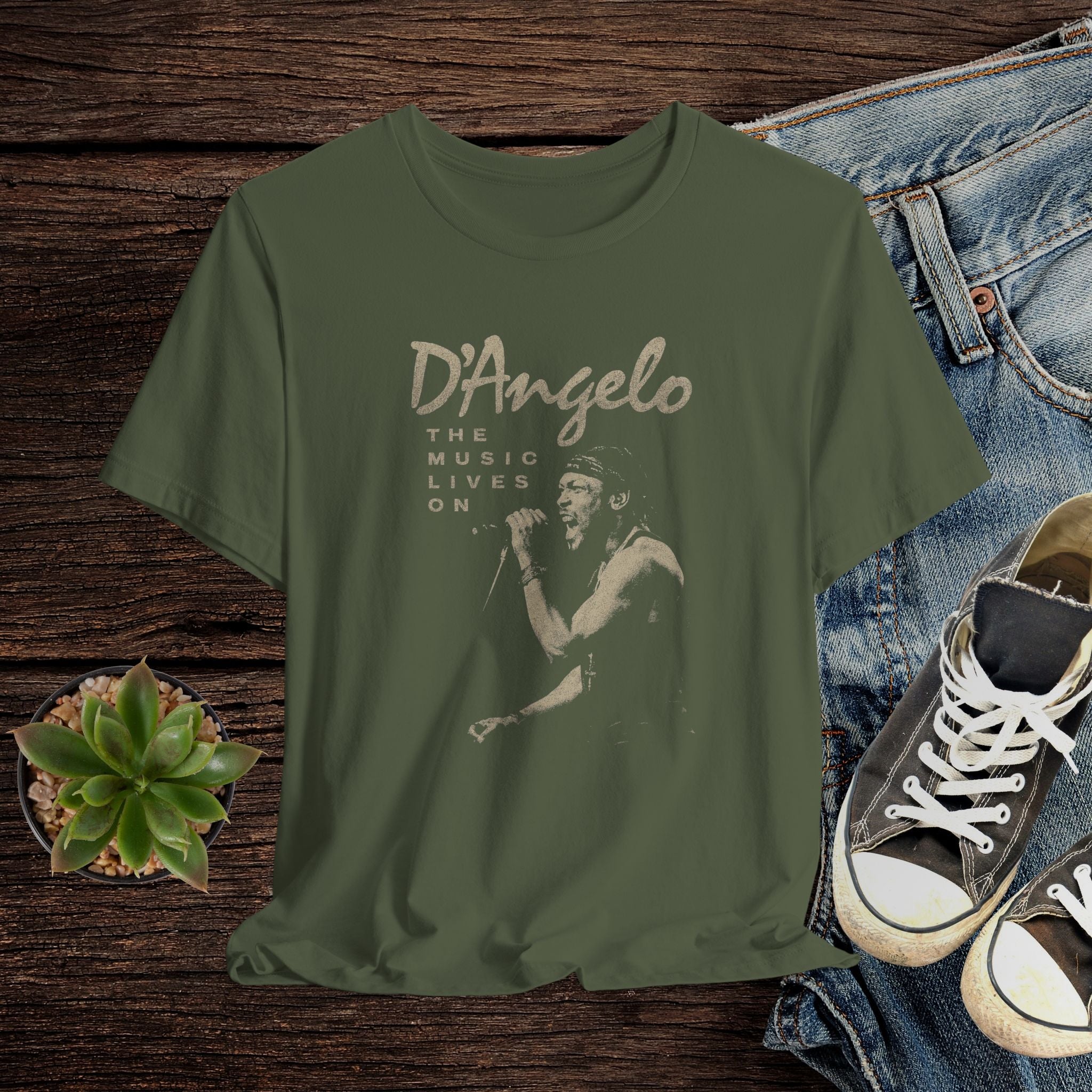 Green t-shirt with 'D'Angelo' graphic design on a wooden surface with jeans and sneakers.