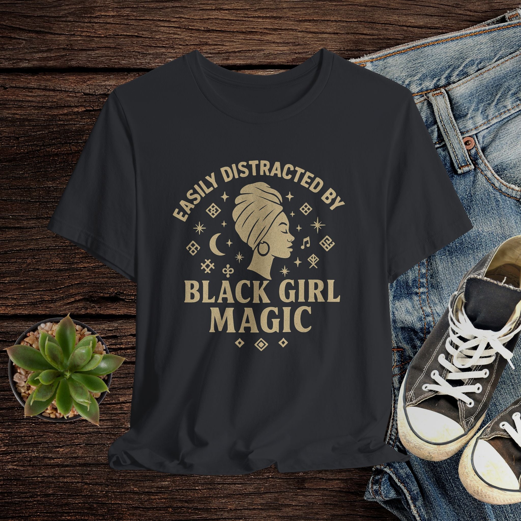 Black t-shirt with 'Easily Distracted by Black Girl Magic' design on a wooden surface with jeans and sneakers.