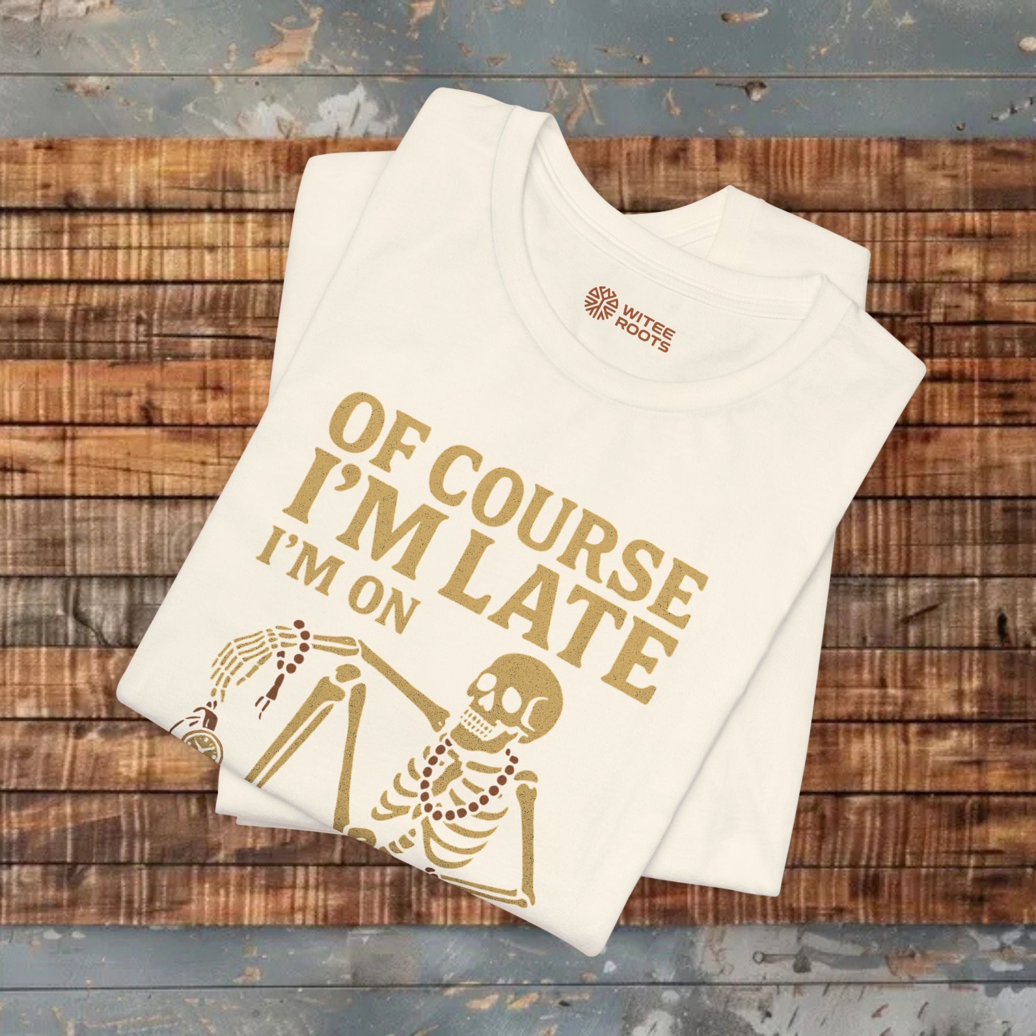 Beige t-shirt with gold text and skeleton design on a wooden surface