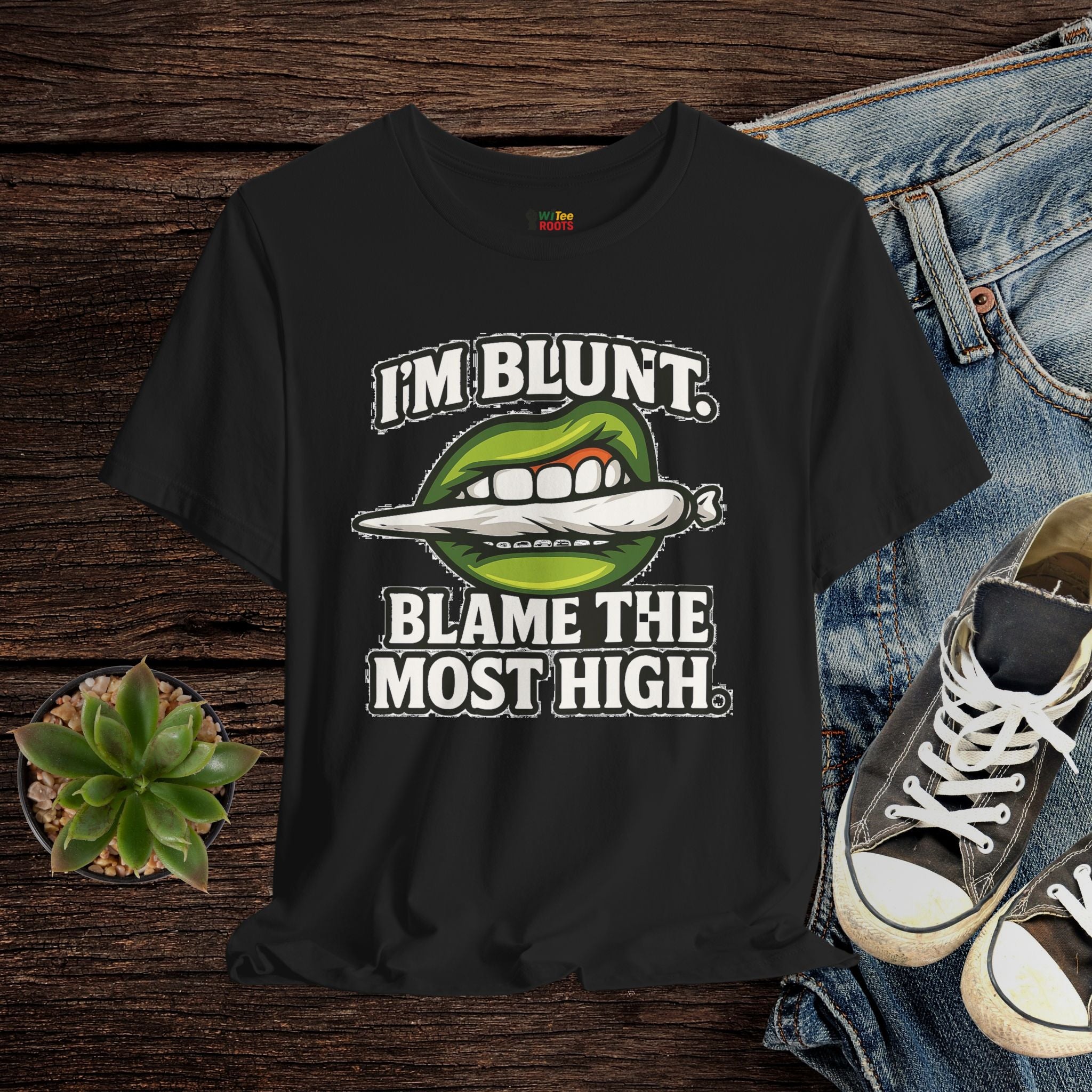 Black t-shirt with graphic design and text on a wooden surface with jeans and sneakers.