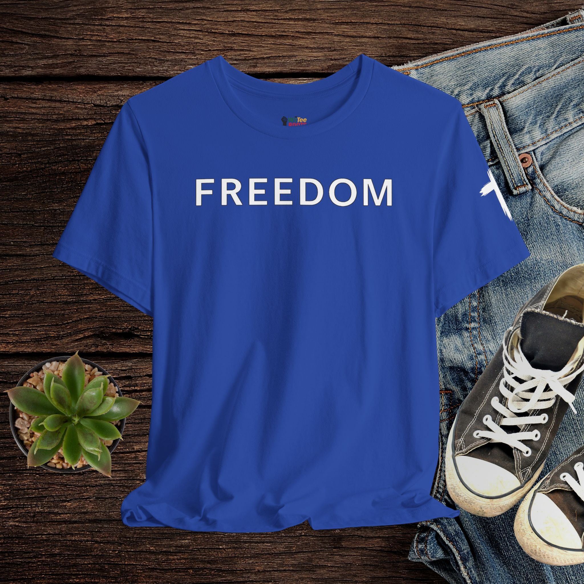 Blue t-shirt with 'FREEDOM' text on a wooden surface with jeans and sneakers.