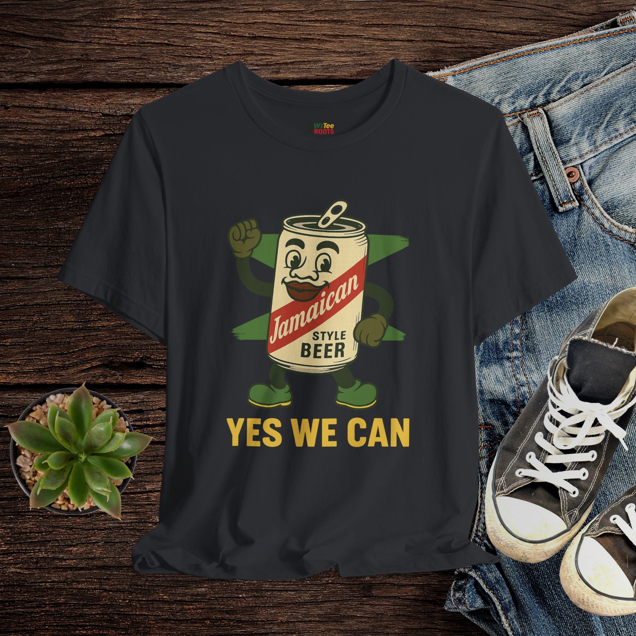 Black t-shirt with Jamaican beer can graphic and 'Yes We Can' text on a wooden surface with jeans and sneakers.