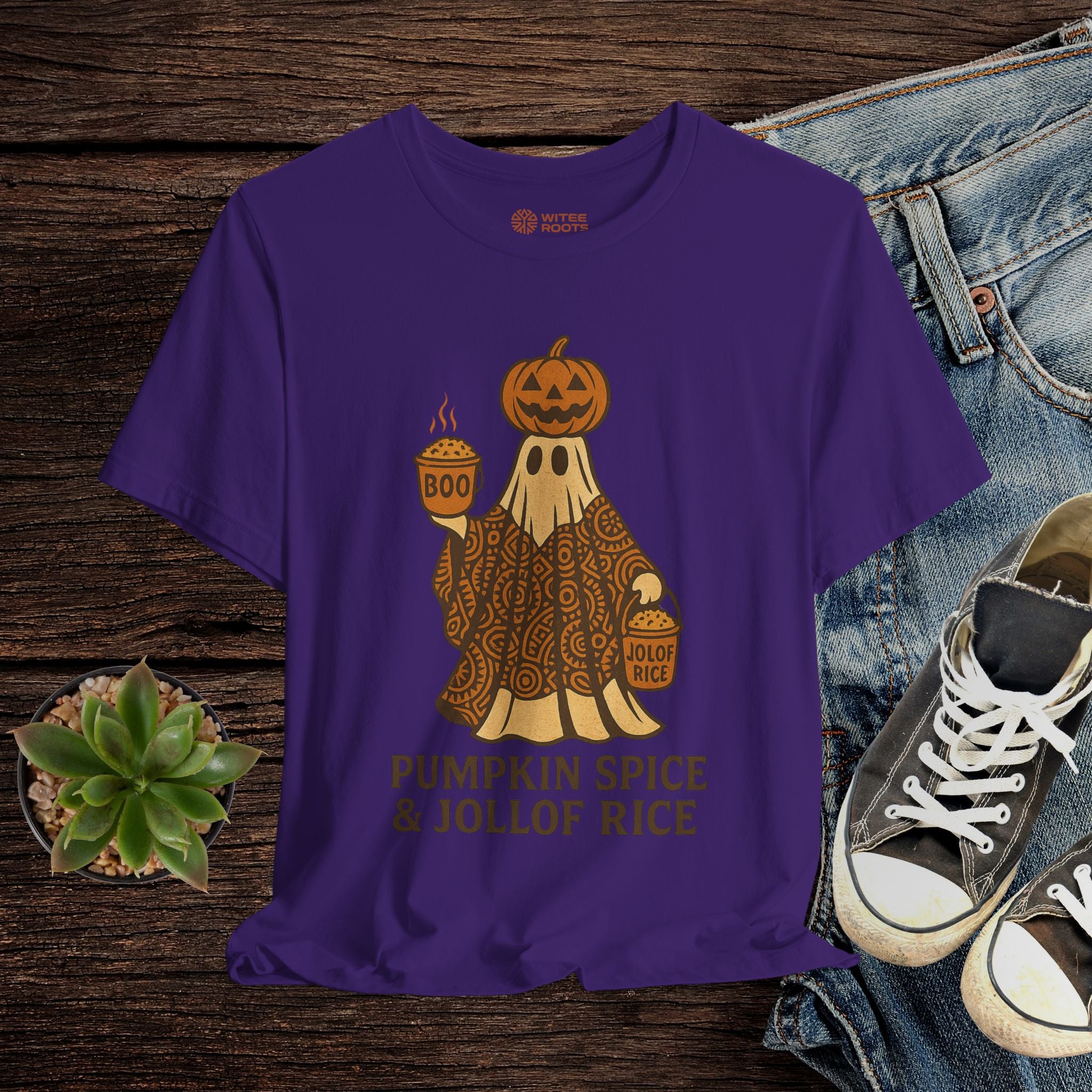 Purple t-shirt with a ghost and pumpkin design on a wooden surface with jeans and sneakers.