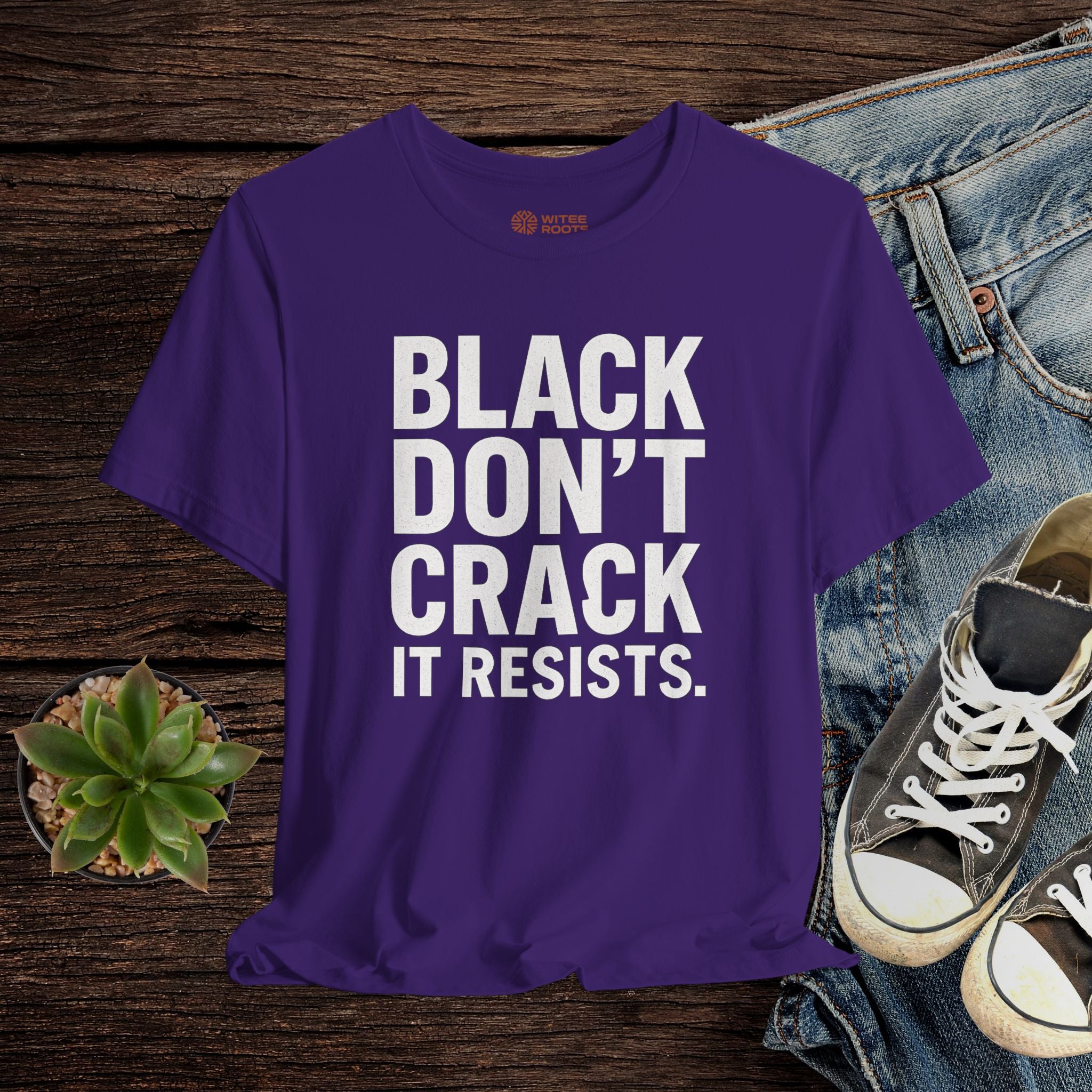 Purple  t-shirt with text on a wooden surface with jeans and sneakers.