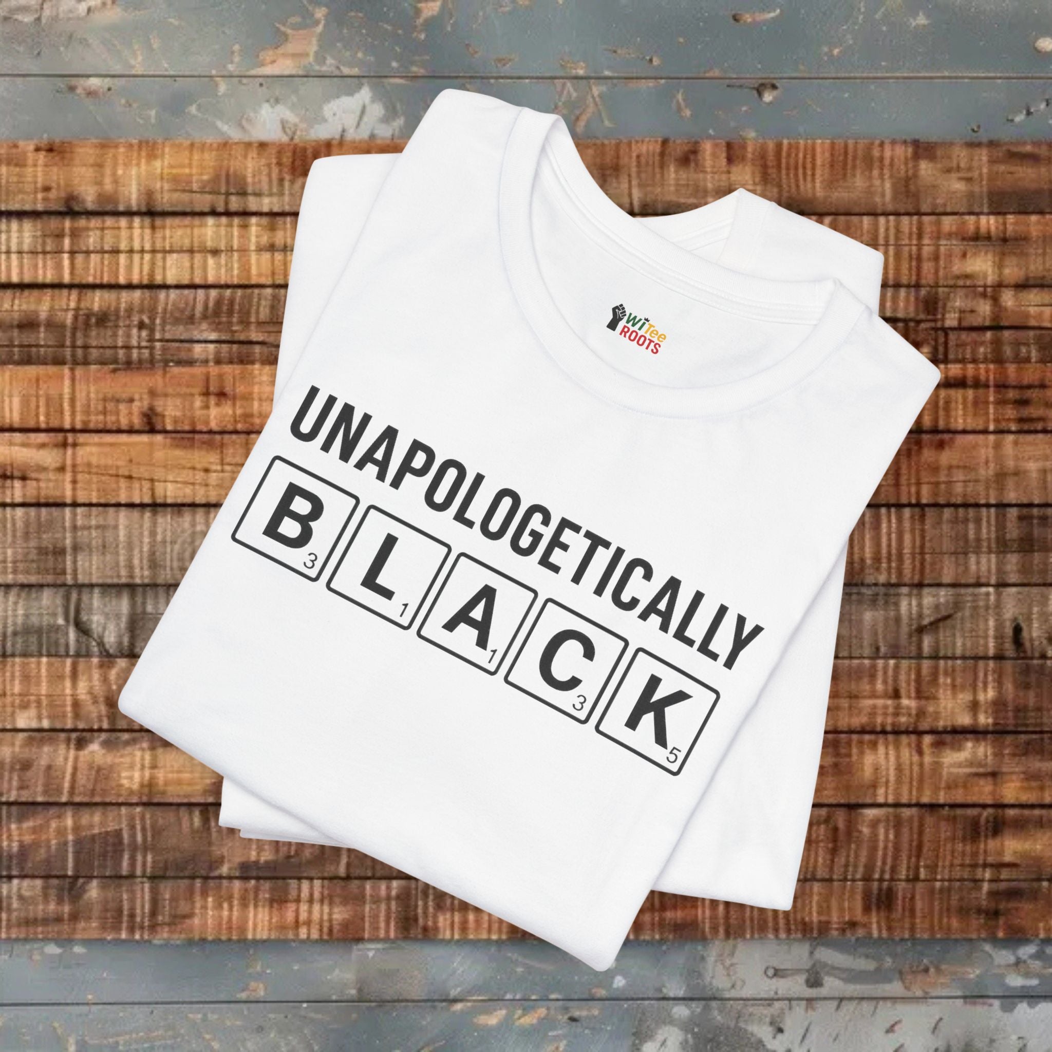 White t-shirt with 'UNAPOLOGETICALLY BLACK' text on a wooden surface