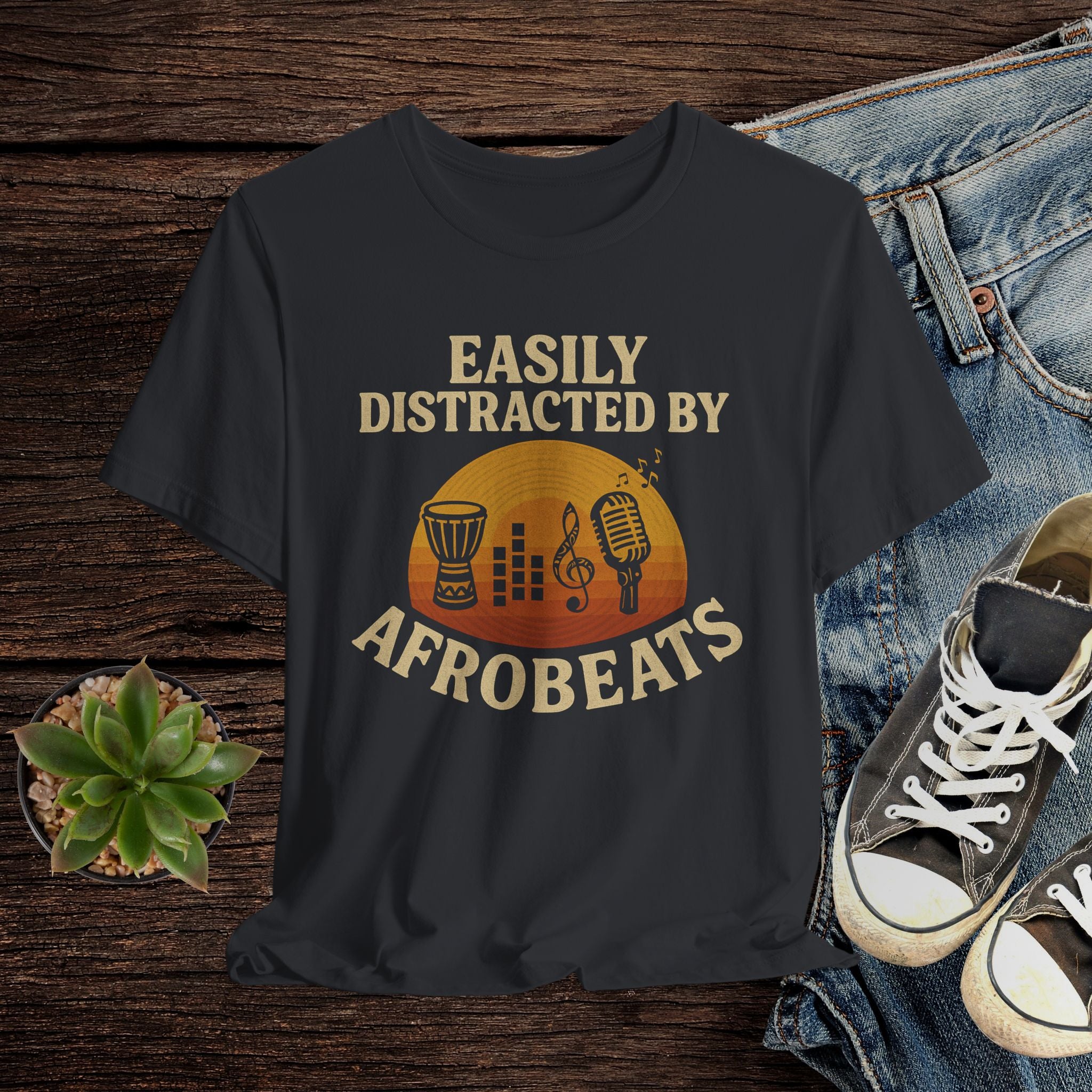 Black t-shirt with 'Easily Distracted by AfroBeats' design on a wooden surface with jeans and sneakers.