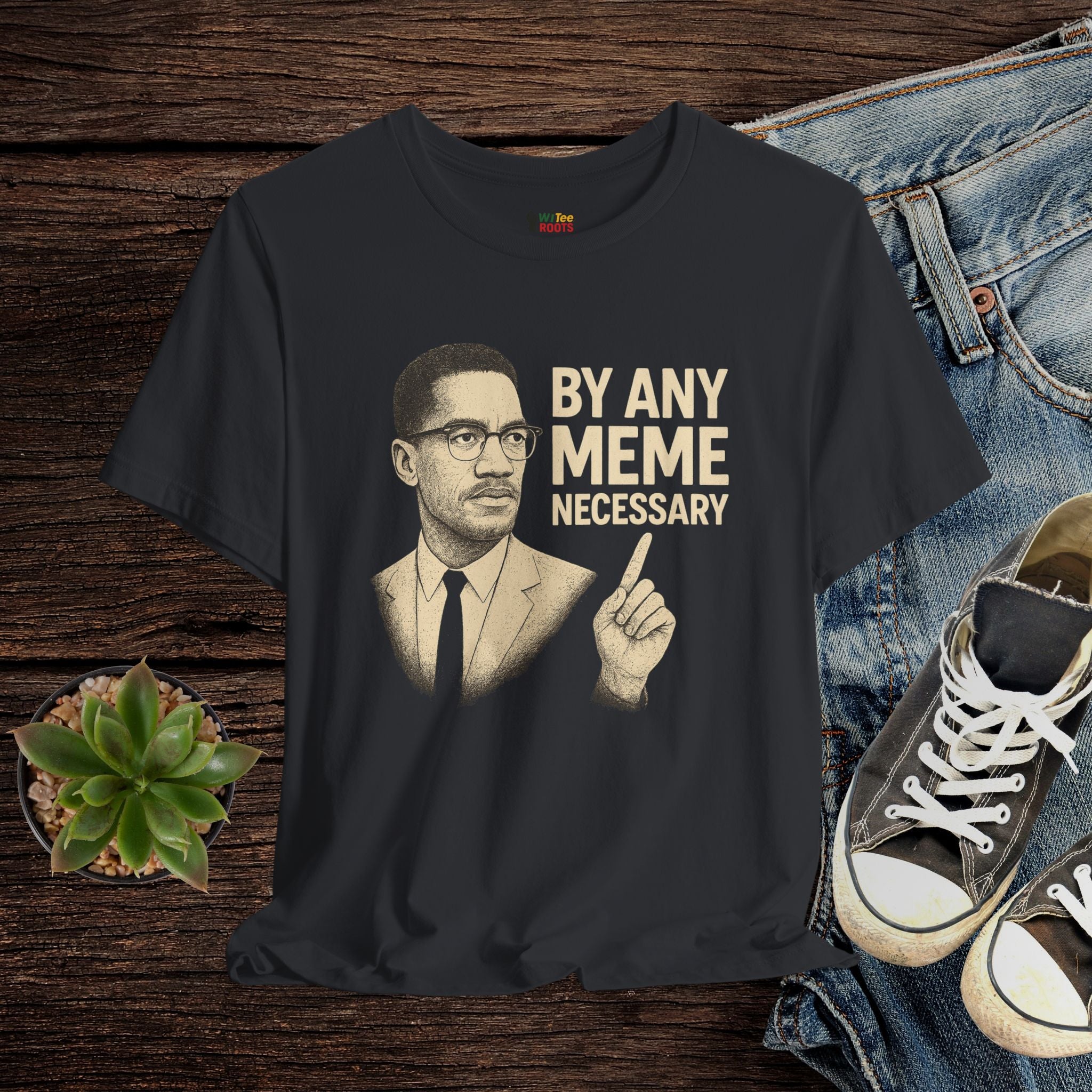 Black t-shirt with a graphic of a man and text 'By Any Meme Necessary' on a wooden surface with jeans and sneakers.