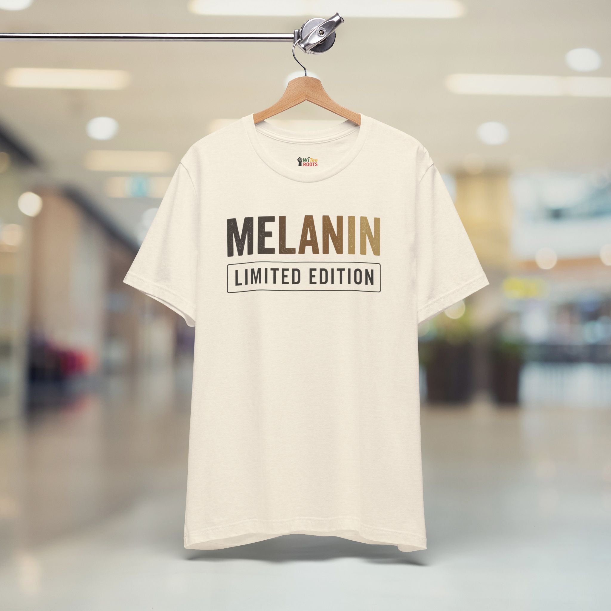 Beige t-shirt with 'MELANIN LIMITED EDITION' text on a hanger in a blurred indoor setting