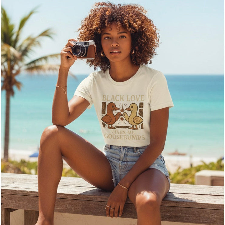 Woman sitting on a bench by the ocean, wearing a t-shirt with a graphic design.