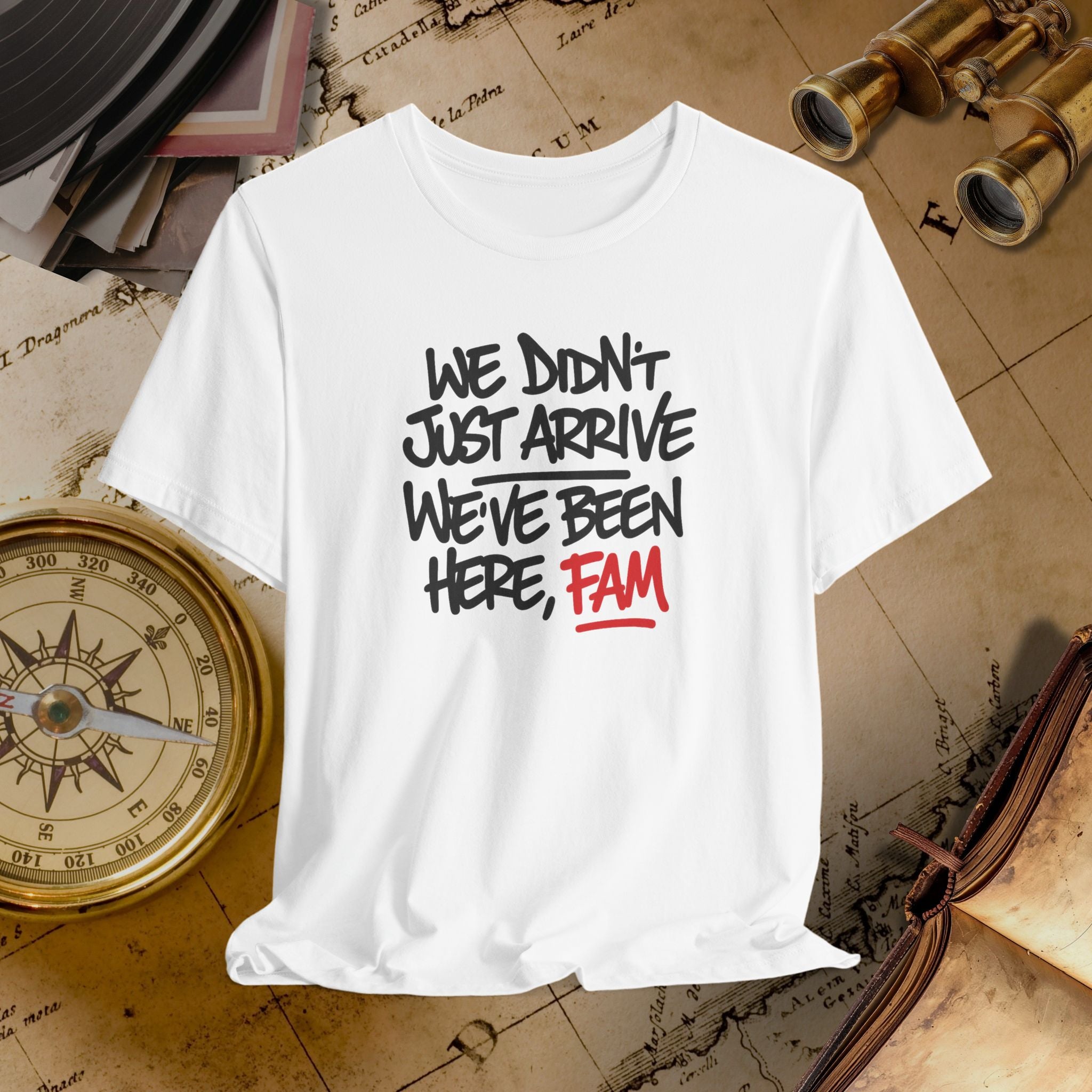 White t-shirt with text 'WE DIDN'T JUST ARRIVE WE'VE BEEN HERE, FAM' on a vintage map background.