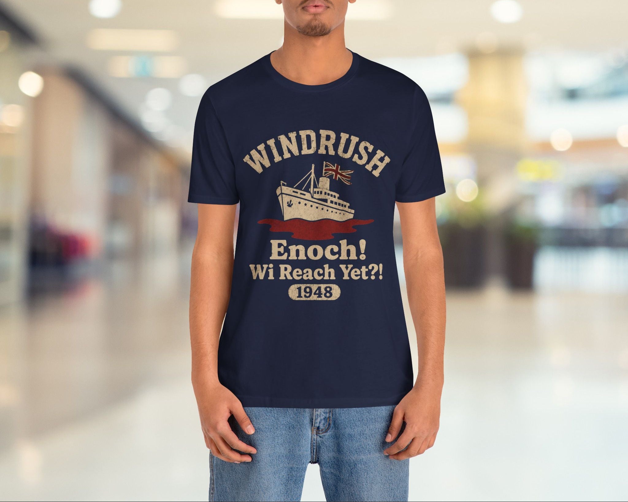 Person wearing a navy blue t-shirt with 'Windrush' design in a blurred indoor setting