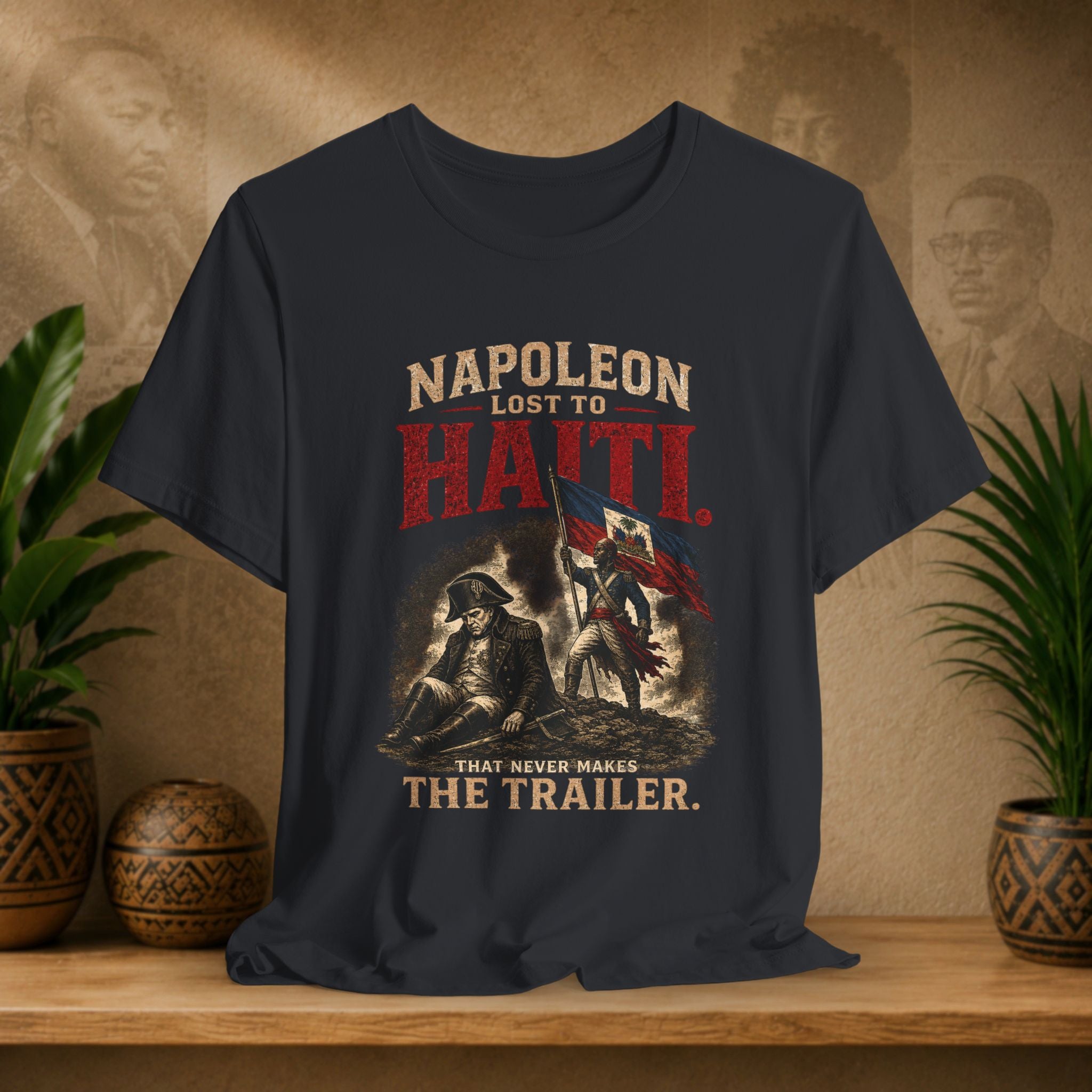 Napoleon Lost to Haiti t-shirt on a wooden surface with decorative plants and background.