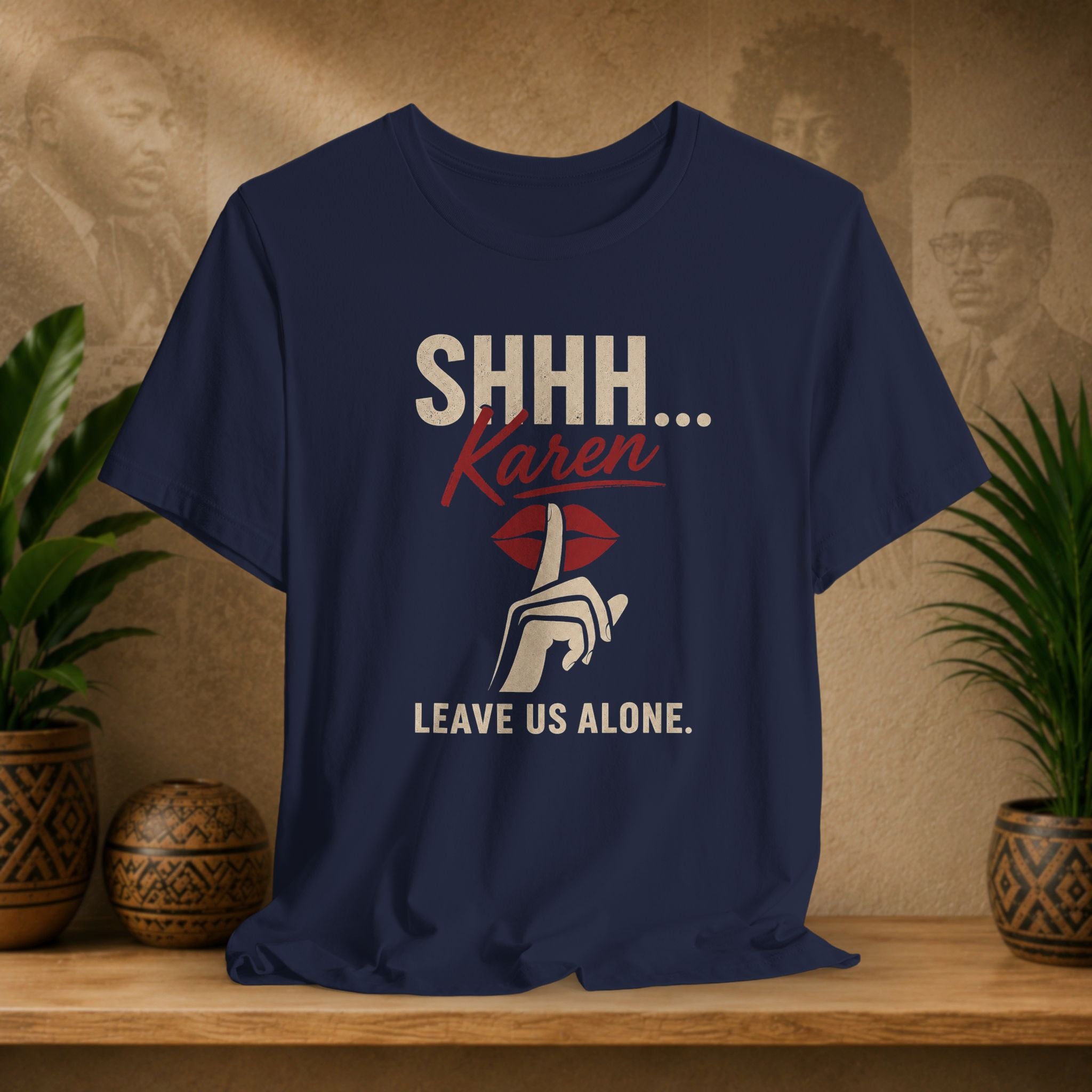 A navy blue graphic t-shirt displayed on a wooden shelf. The shirt features a graphic print with the text 'SHHH.