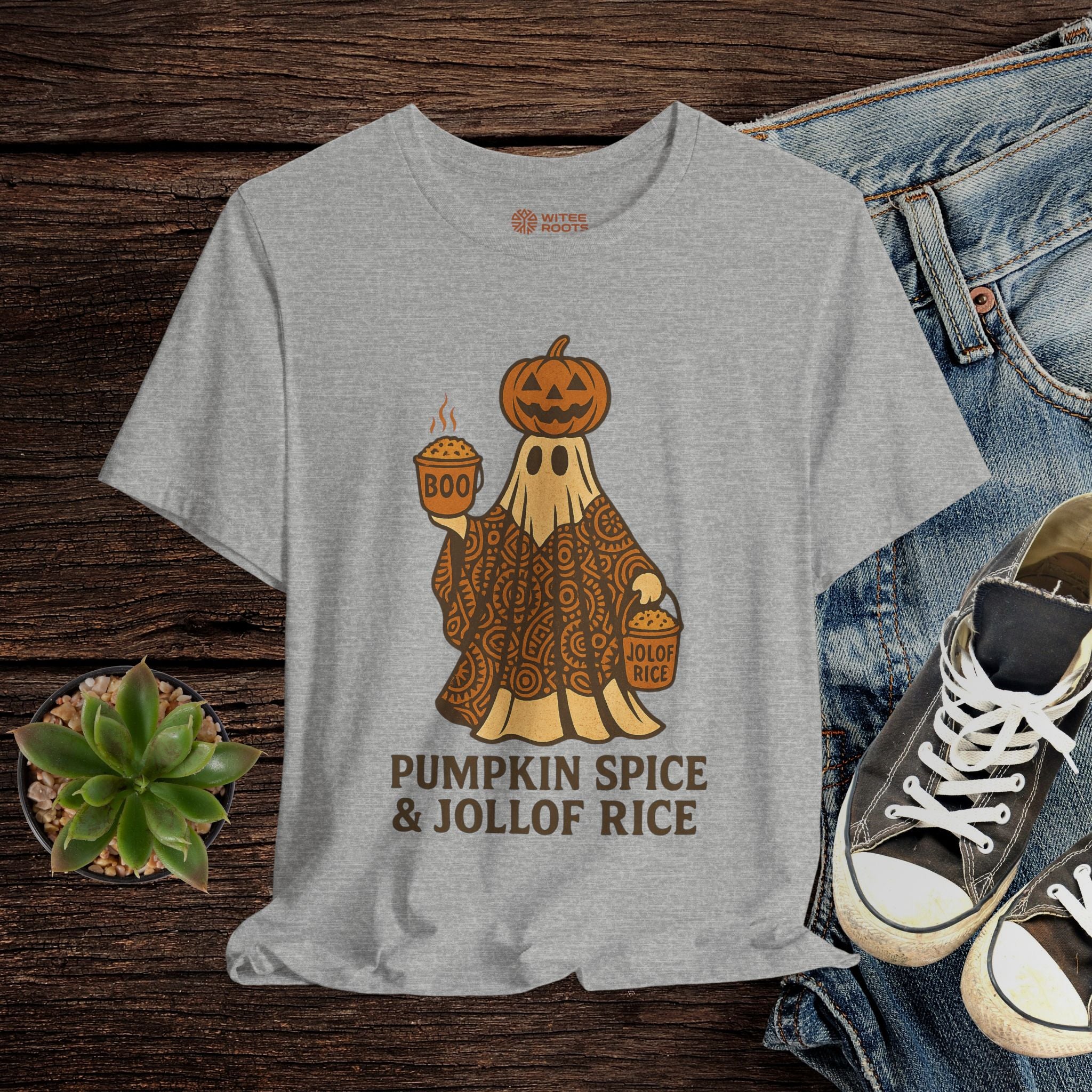 Gray t-shirt with a ghost holding pumpkins and text 'Pumpkin Spice & Jollof Rice' on a wooden surface with jeans and sneakers.