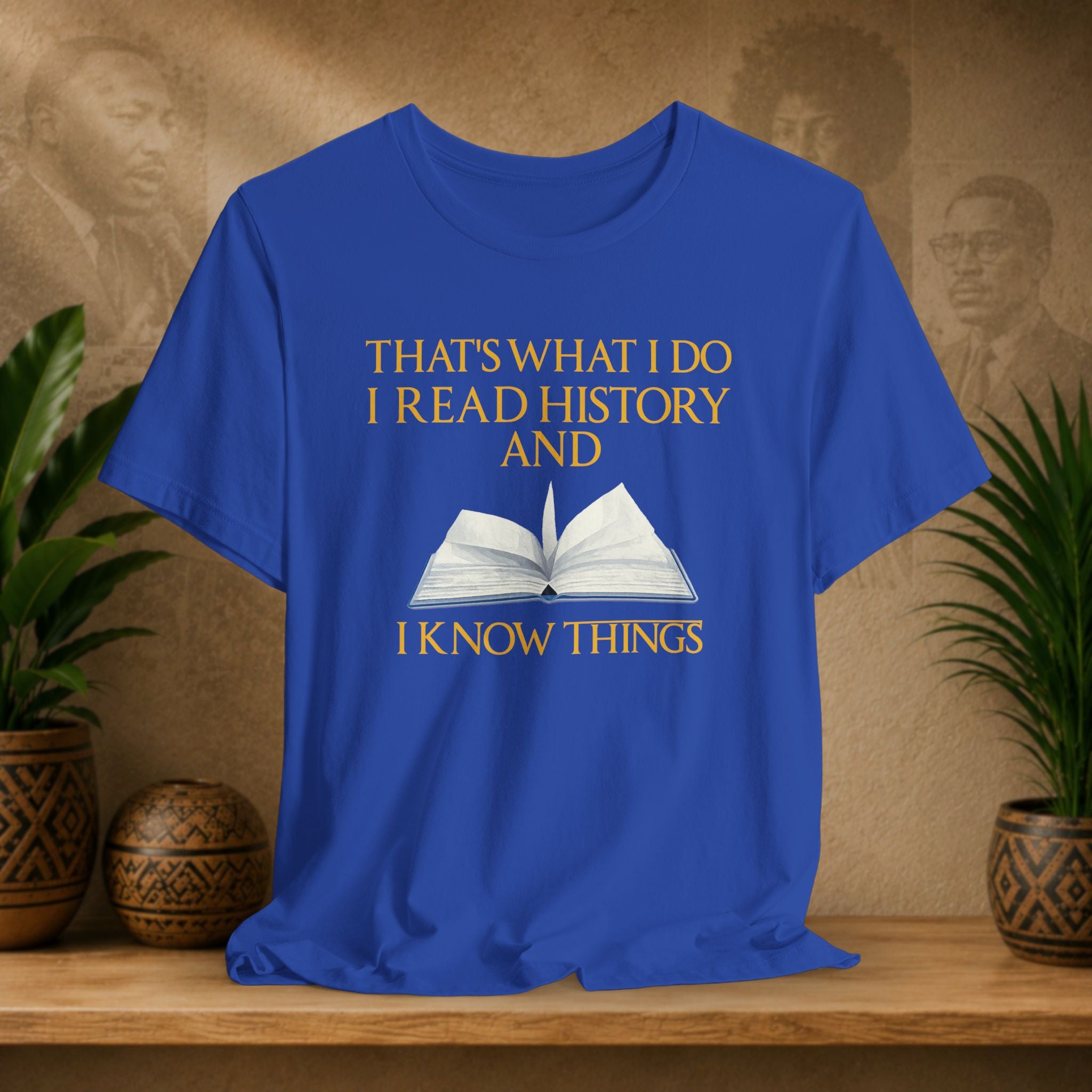 Blue t-shirt with text and book graphic on a wooden surface with plants and decorative items.